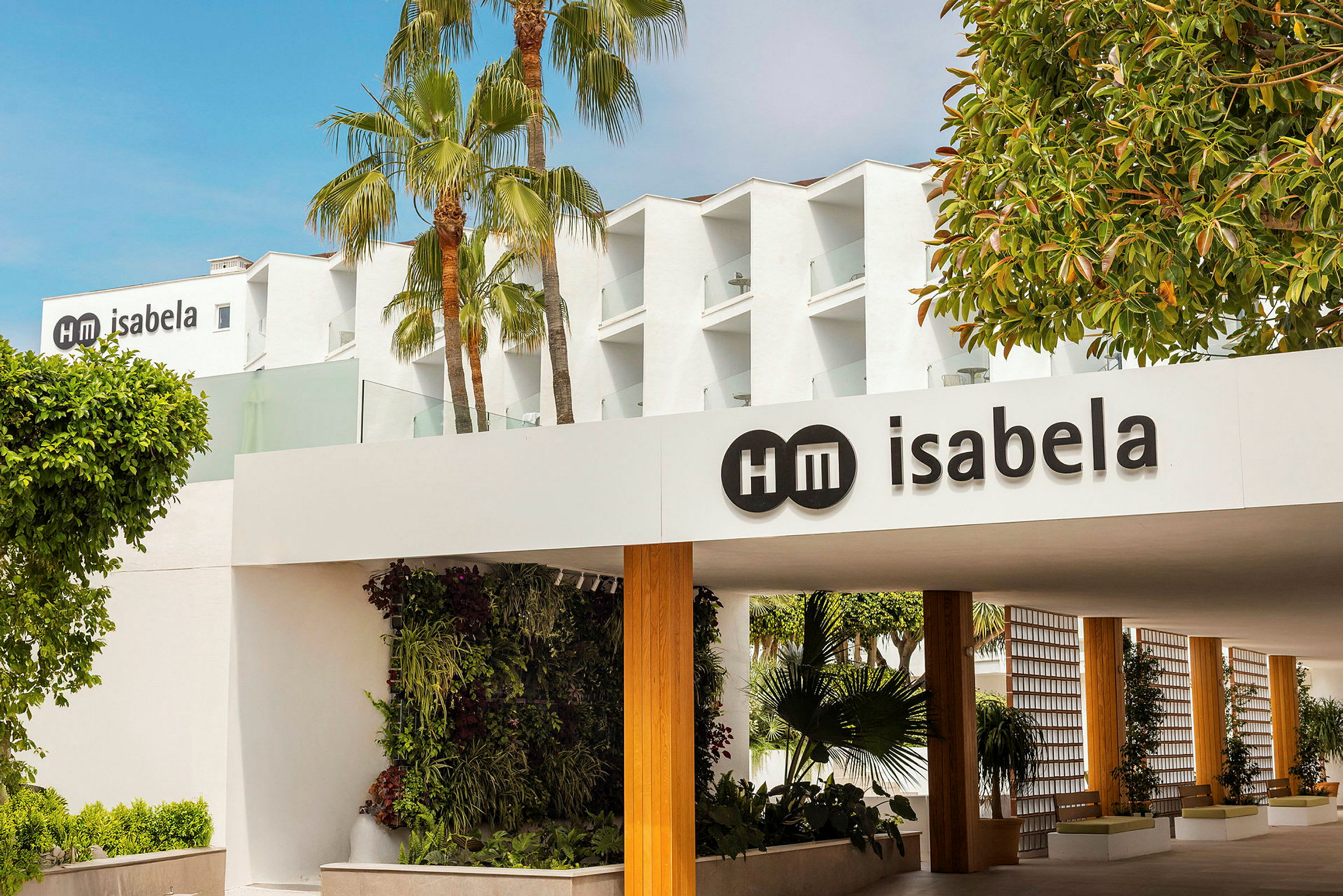 Billede af en hotelbygning med navnet "HM Isabela" synligt på skiltet. Palme- og grønne områder ses omkring bygningen. (AI-genereret tekst)