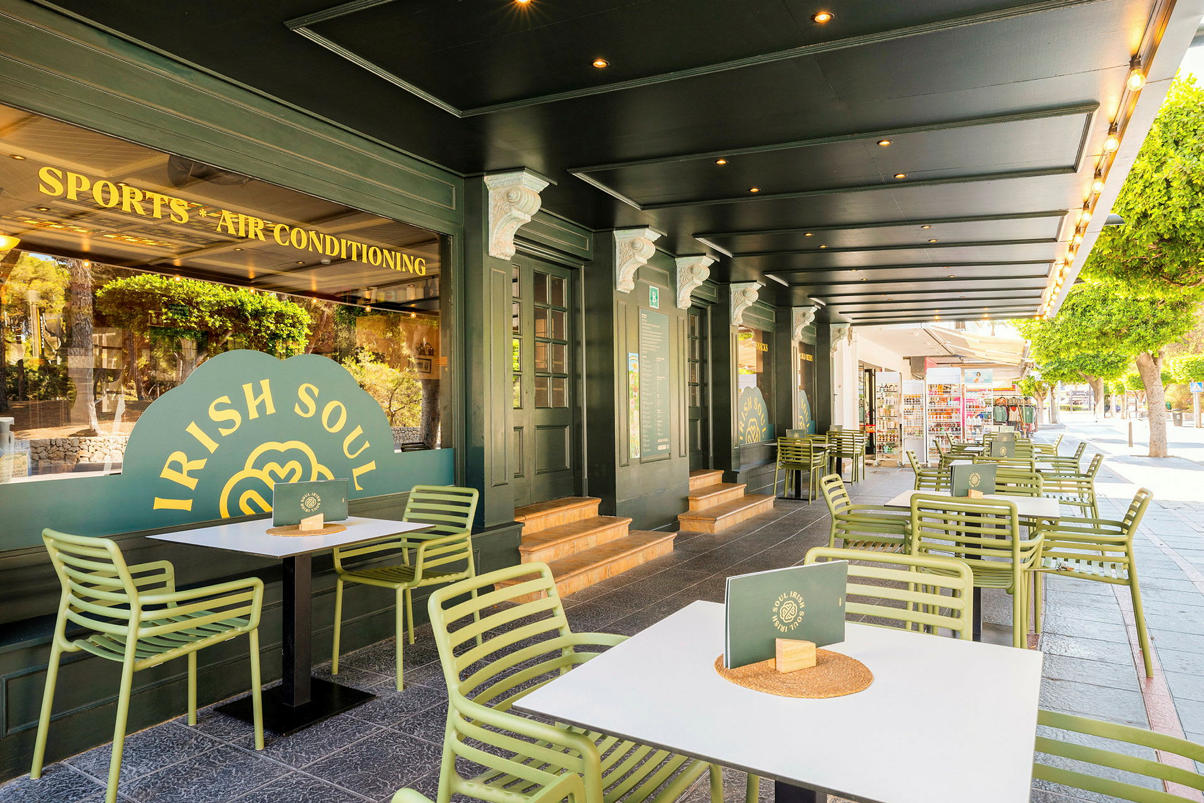 Udendørs servering med grønne stole og hvide borde foran en restaurant med grøn facade. (AI-genereret tekst)