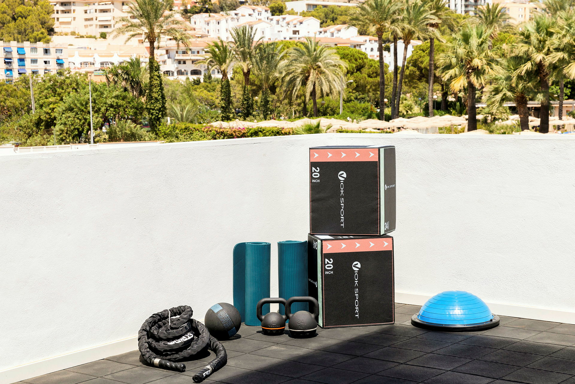 Træningsudstyr inklusive bokse, træningsmåtter, kettlebells og en balancebold på en terrasse. (AI-genereret tekst)