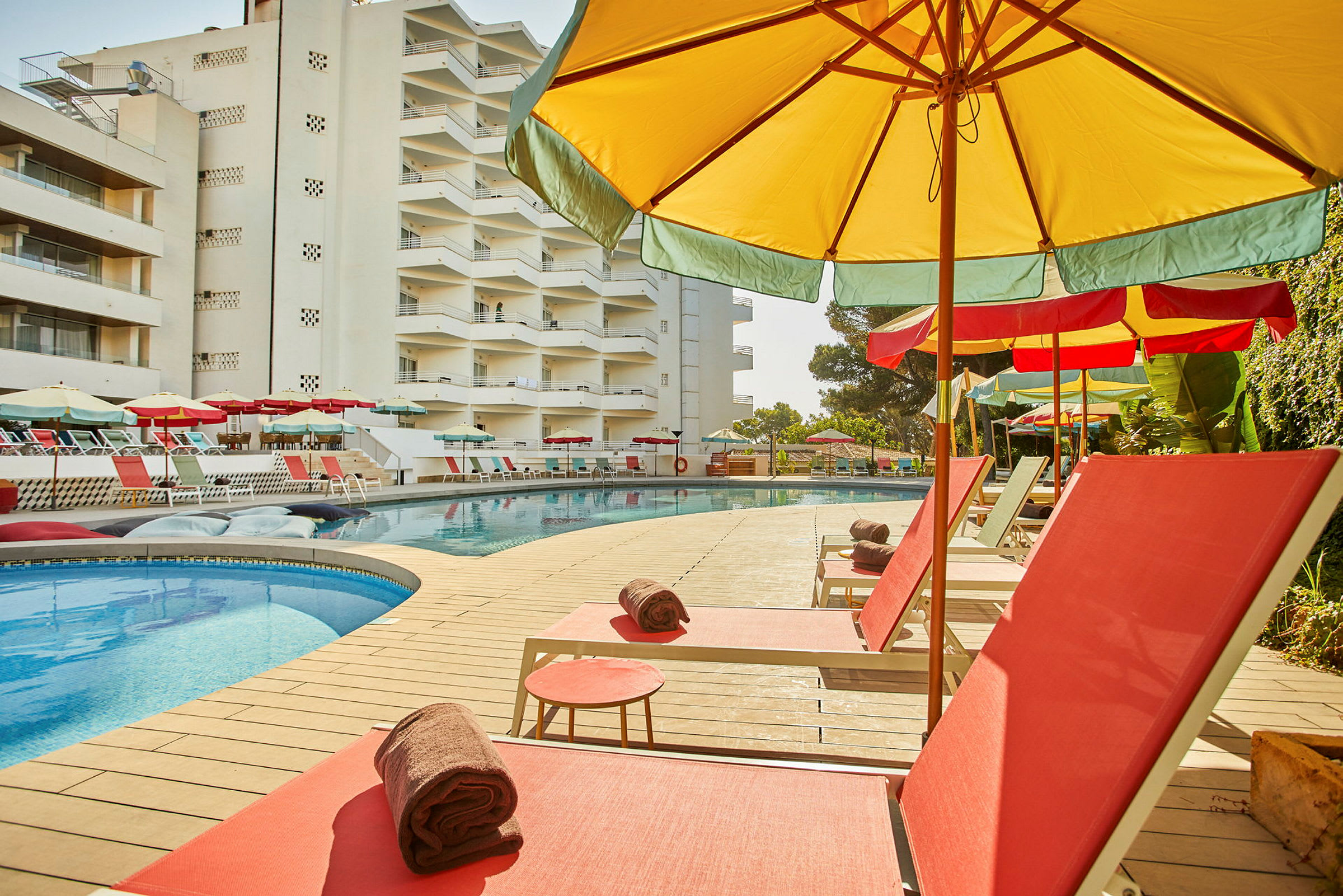Liggestole og parasoller ved en swimmingpool ved siden af et hotel. (AI-genereret tekst)