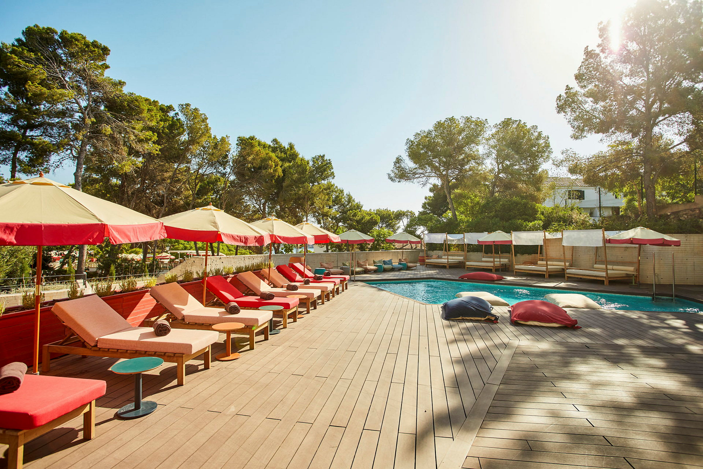 En solterrasse med liggestole og parasoller ved siden af en pool, omgivet af grønne omgivelser. (AI-genereret tekst)
