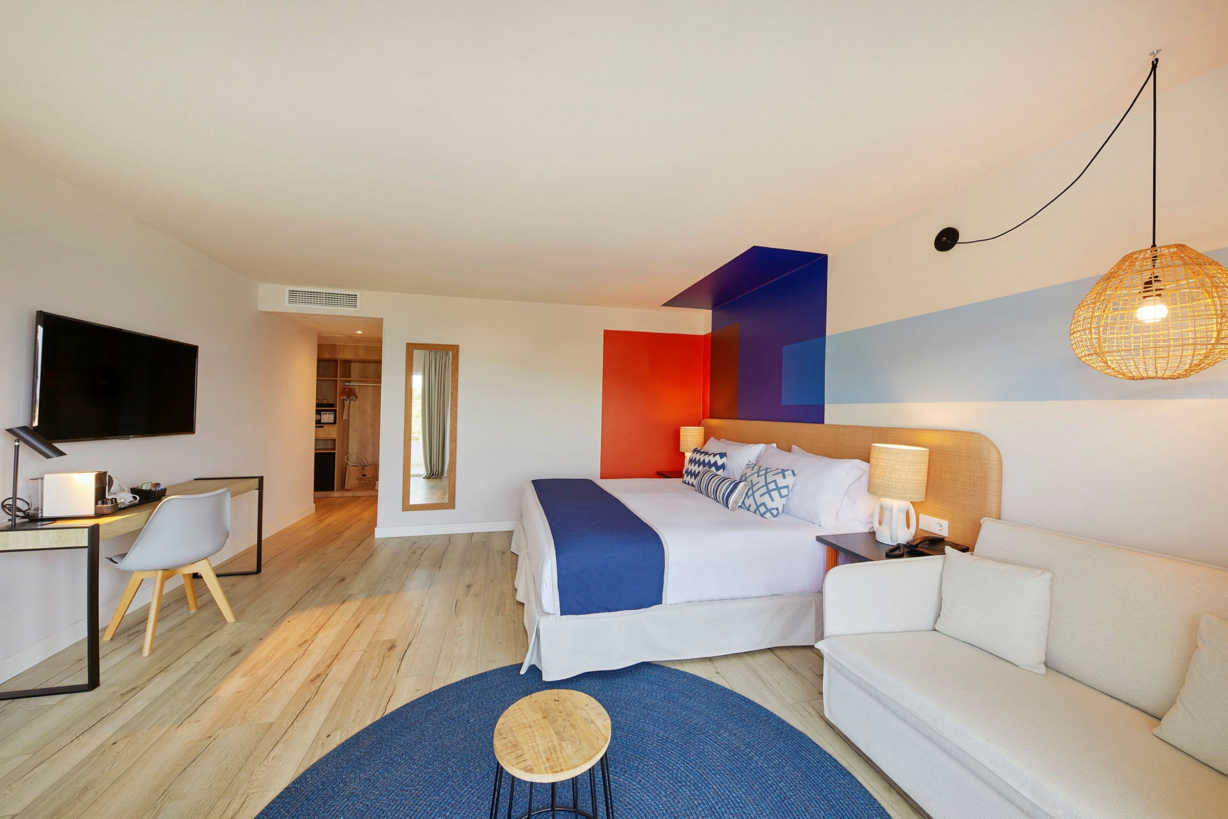 Et moderne hotelværelse med en behagelig seng, en skrivebordskrog og et siddeområde, indrettet med farverige detaljer. (AI-genereret tekst)