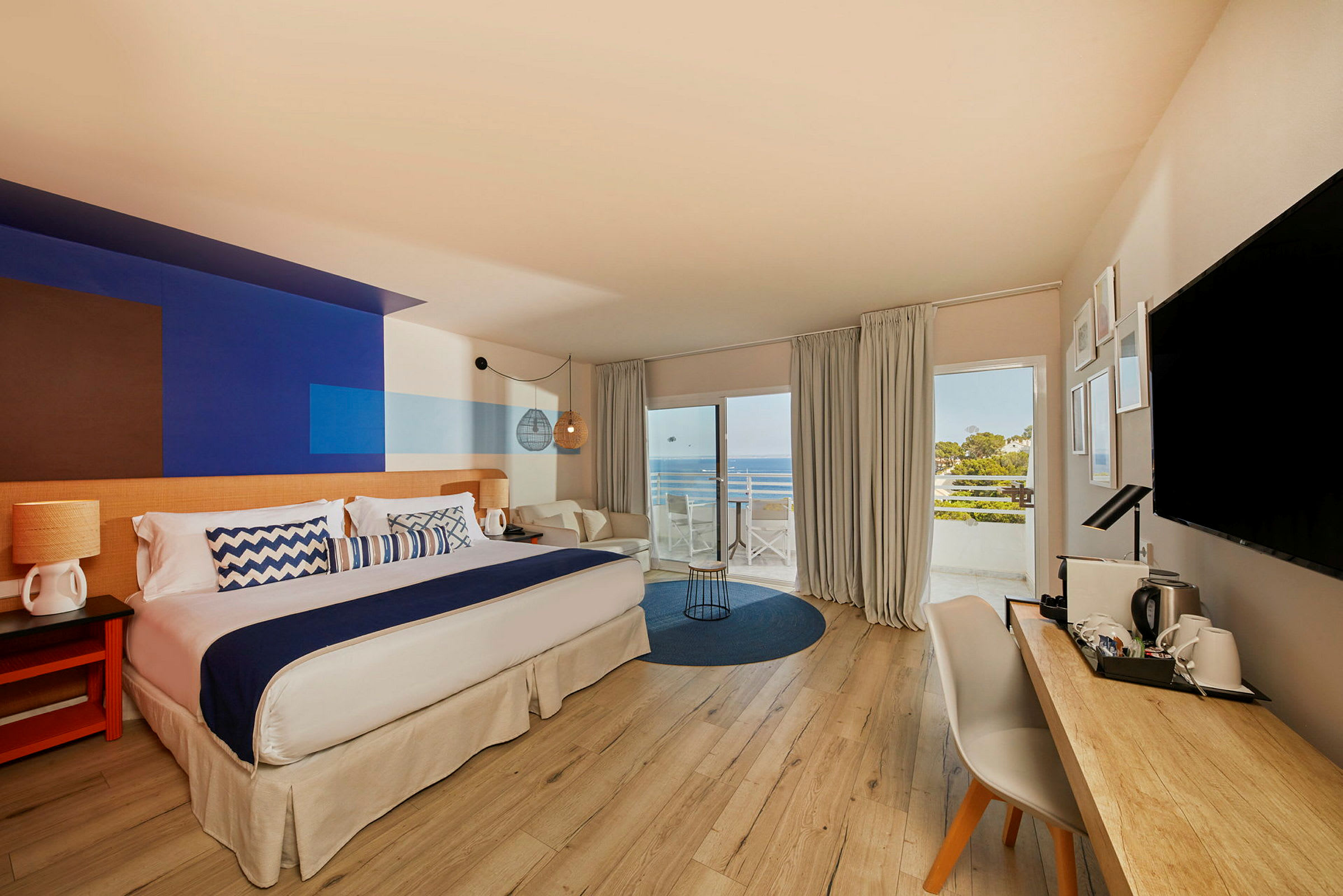 Et hotelværelse med stor seng, skrivebord og udsigt over havet fra altan. (AI-genereret tekst)