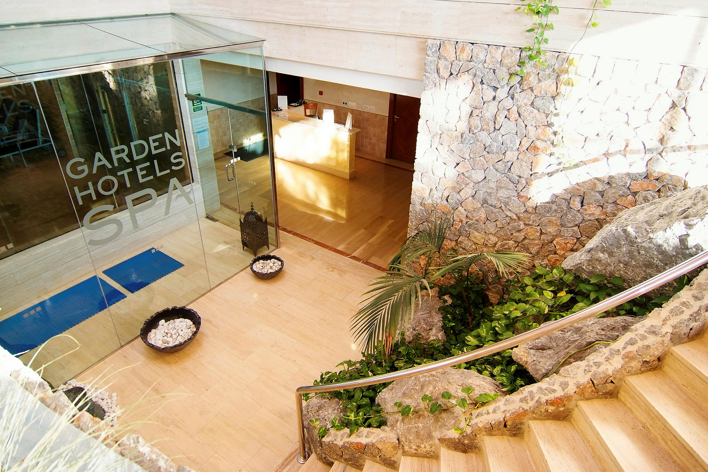 Reception med glasdør mærket "Garden Hotels Spa", stenmur og trappe. (AI-genereret tekst)