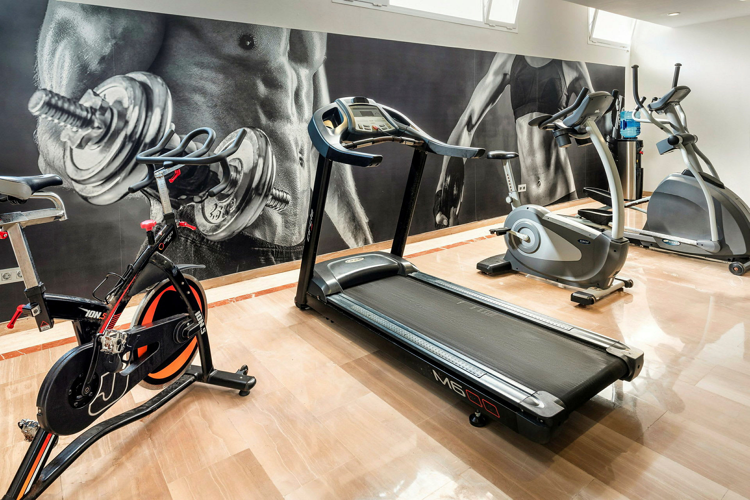 Et fitnesscenter med motionscykel, løbebånd og crosstrainer. (AI-genereret tekst)
