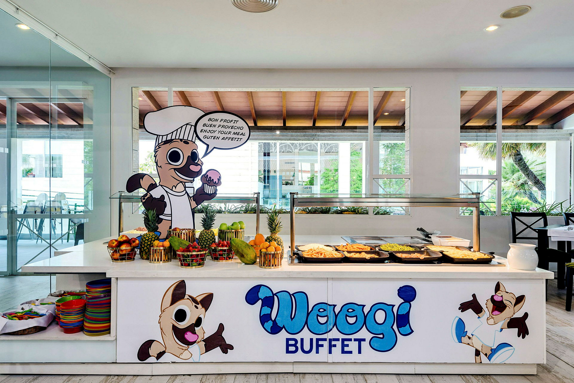 Buffetbord med forskellige retter, frisk frugt og tegneseriefigurer med teksten 'Woogi Buffet'. (AI-genereret tekst)