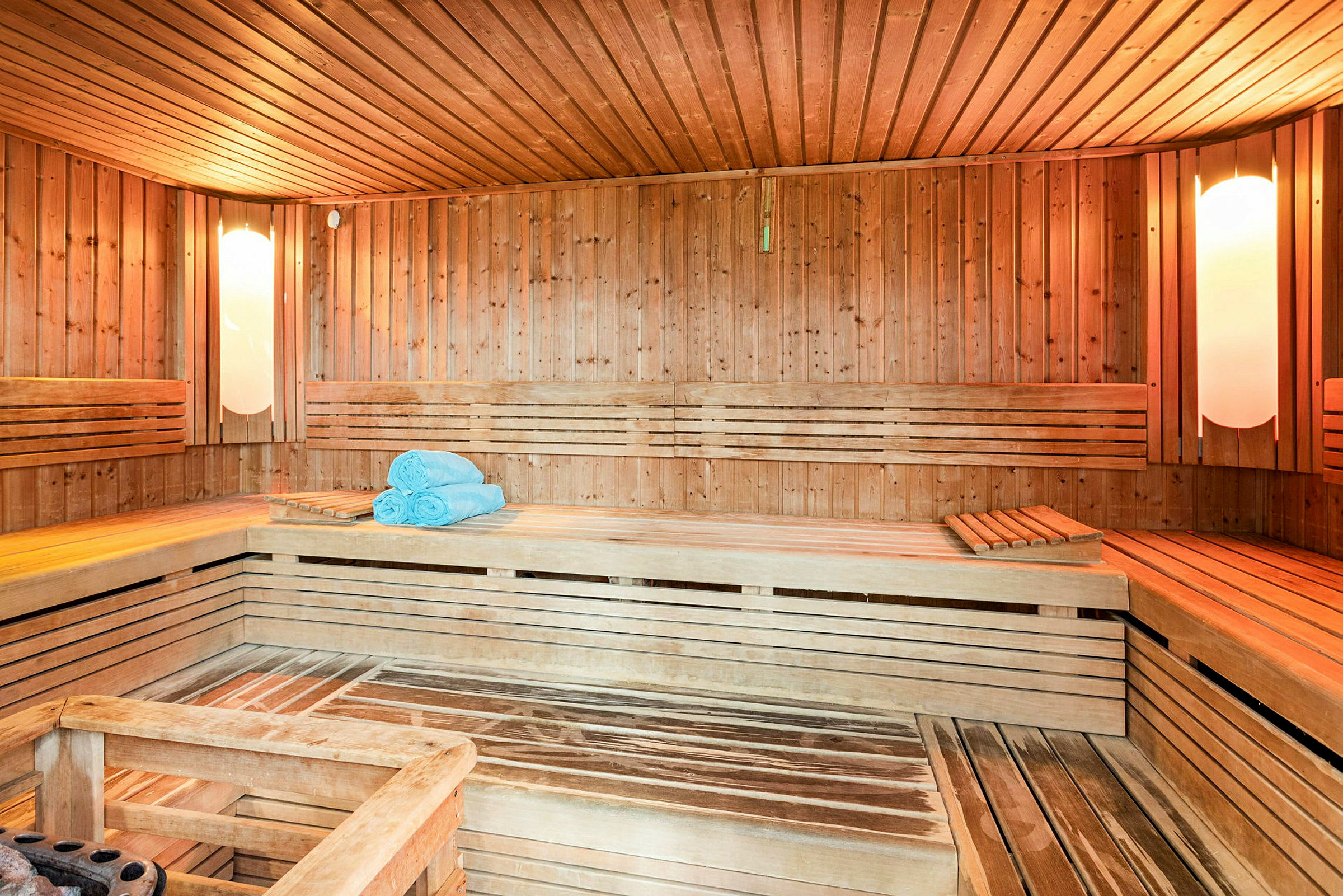 En sauna med træpaneler, siddebænke og blå håndklæder placeret på en af bænkene. (AI-genereret tekst)