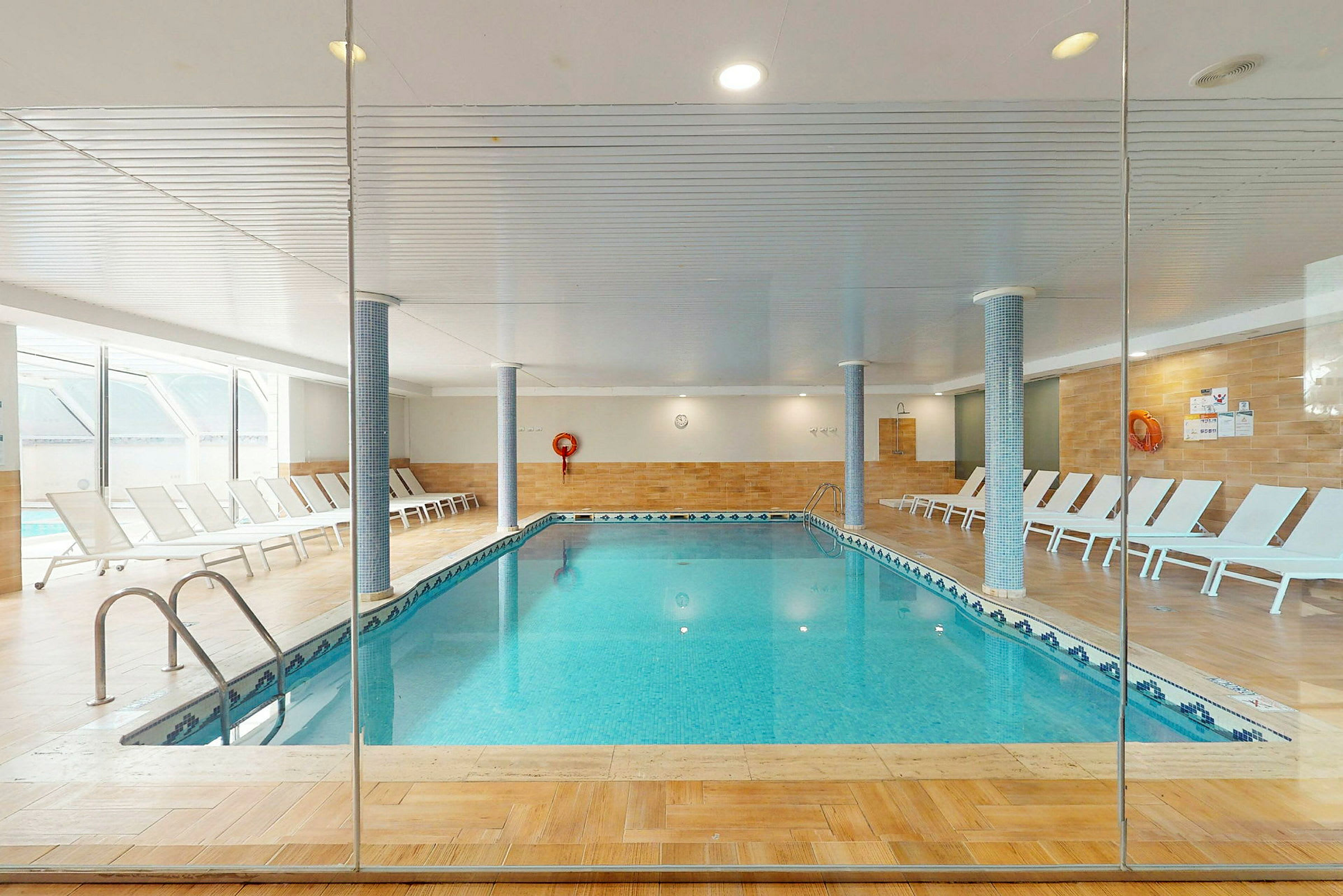Indendørs swimmingpool med liggestole langs kanterne. (AI-genereret tekst)