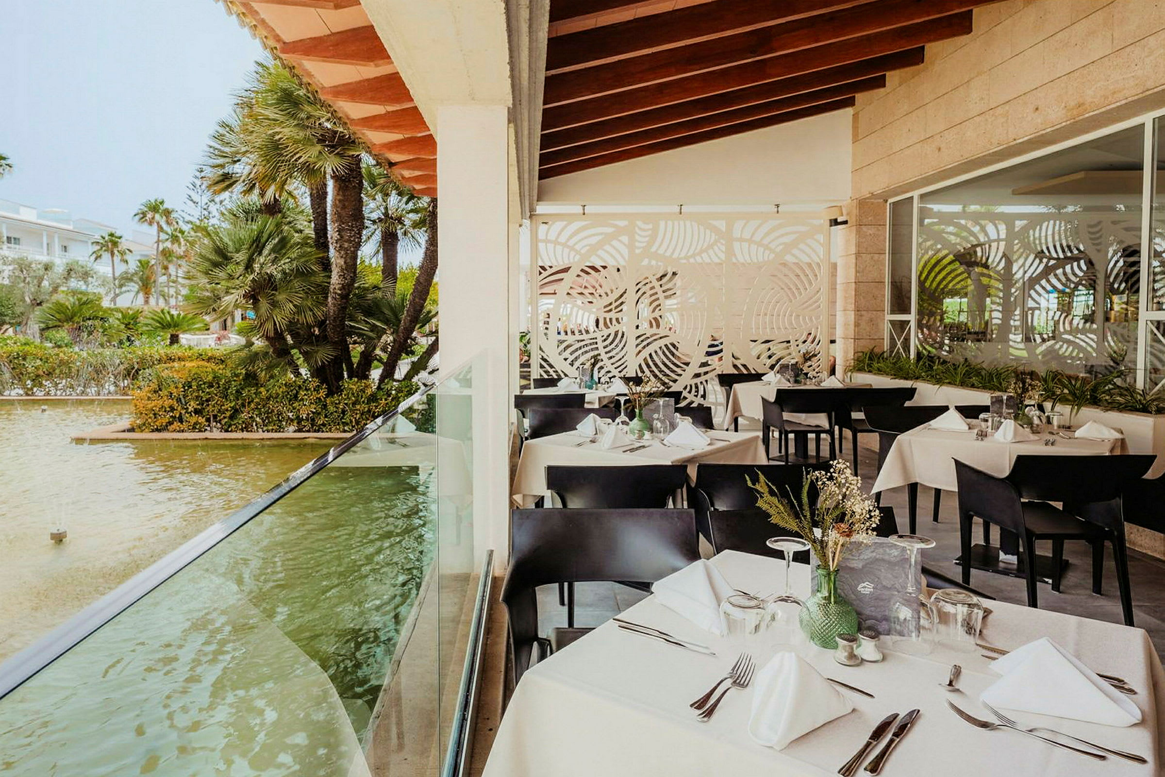 Restaurant med siddepladser tæt på et lille dam omgivet af planter. (AI-genereret tekst)