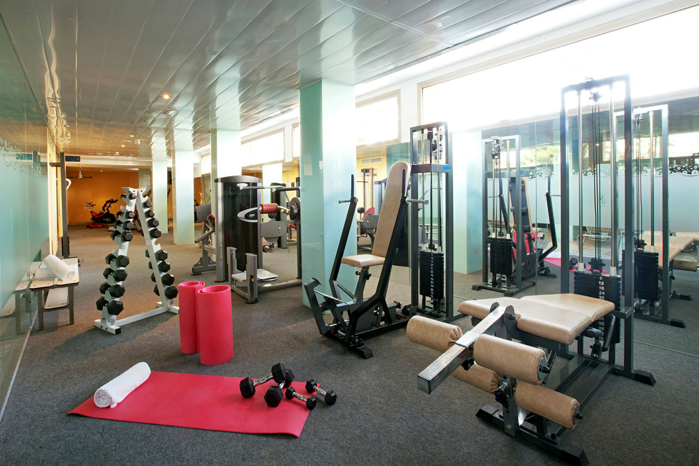 Fitnesscenter med træningsudstyr, herunder maskiner, vægte og træningsmåtter. (AI-genereret tekst)