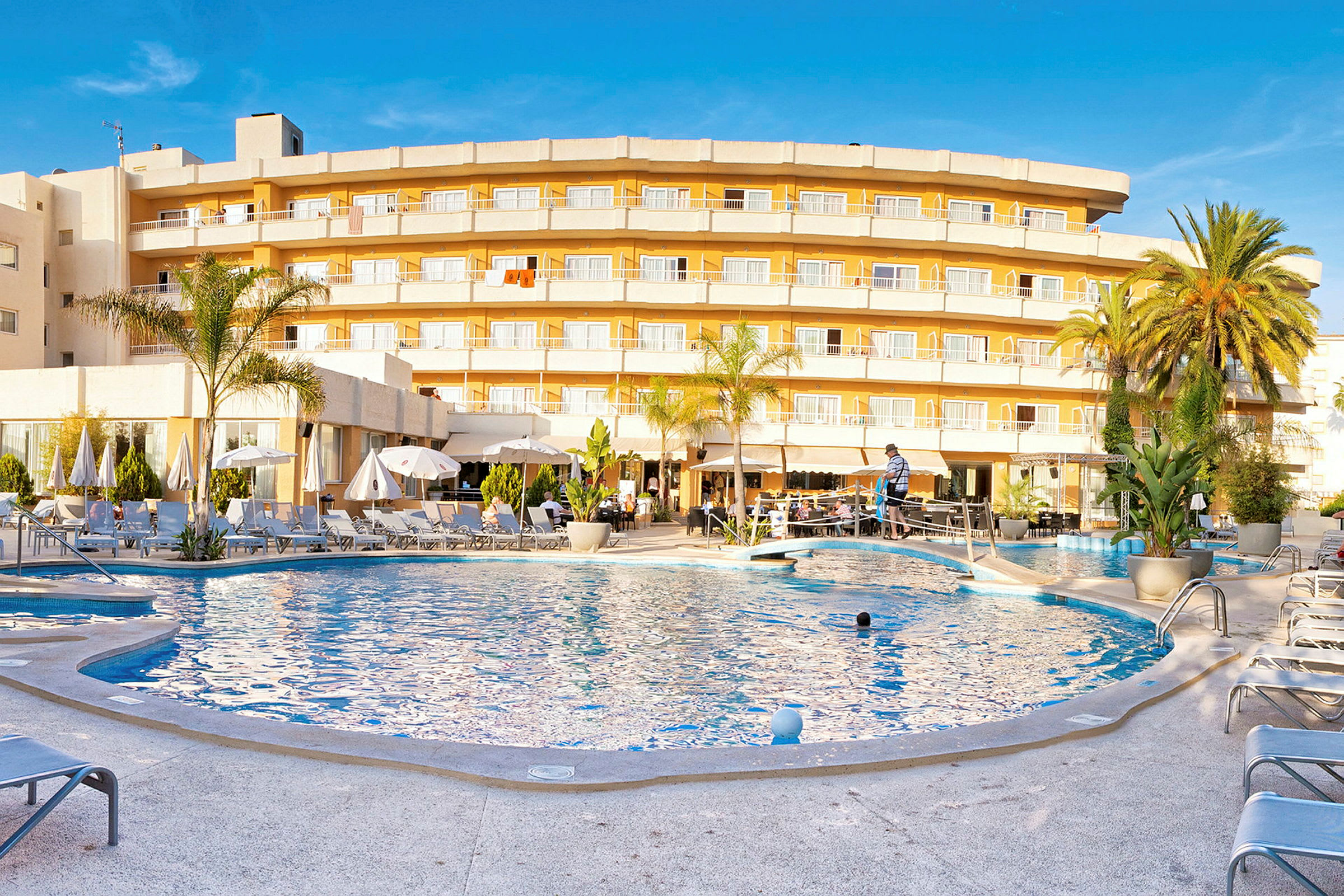 Hotel med gul facade og altaner foran en swimmingpool omgivet af liggestole. (AI-genereret tekst)