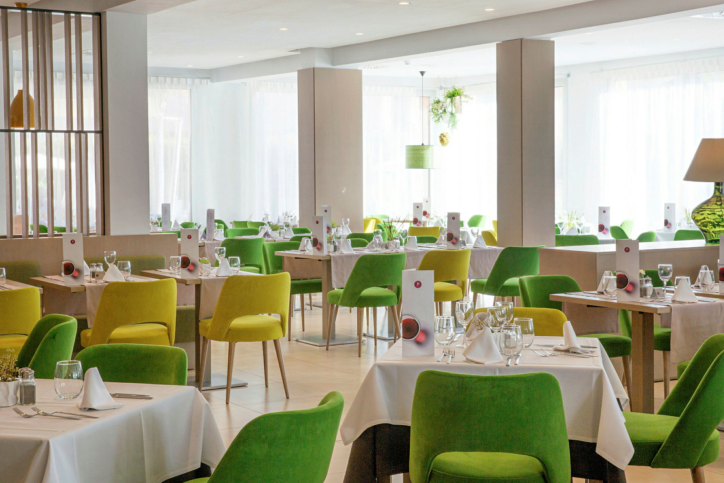 Et lyst og moderne restaurantområde med grønne og gule stole og dækkede borde. (AI-genereret tekst)