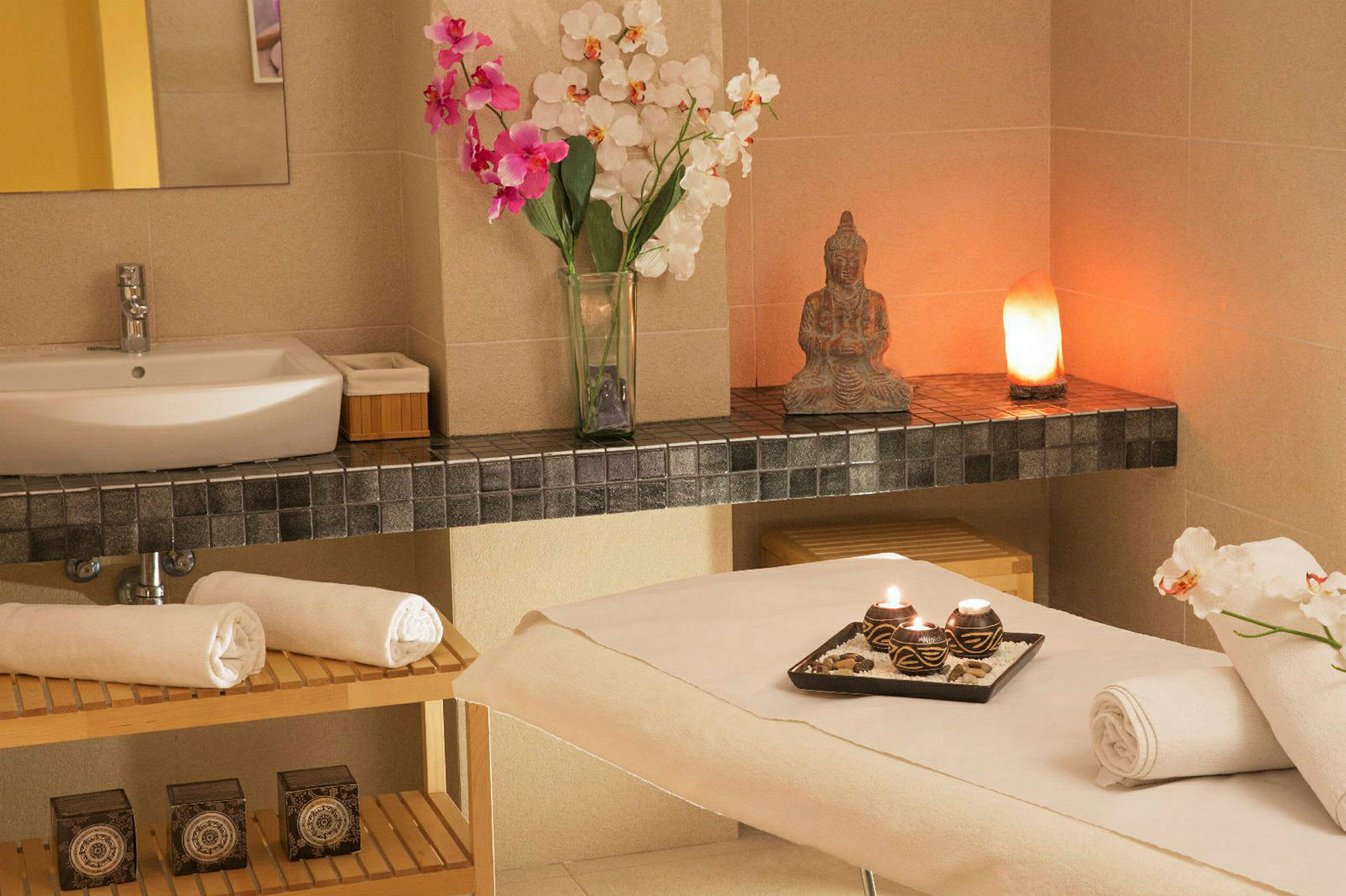Et indbydende spa-rum med massagebriks, håndklæder og en bakke med tændte lys samt en håndvask. (AI-genereret tekst)