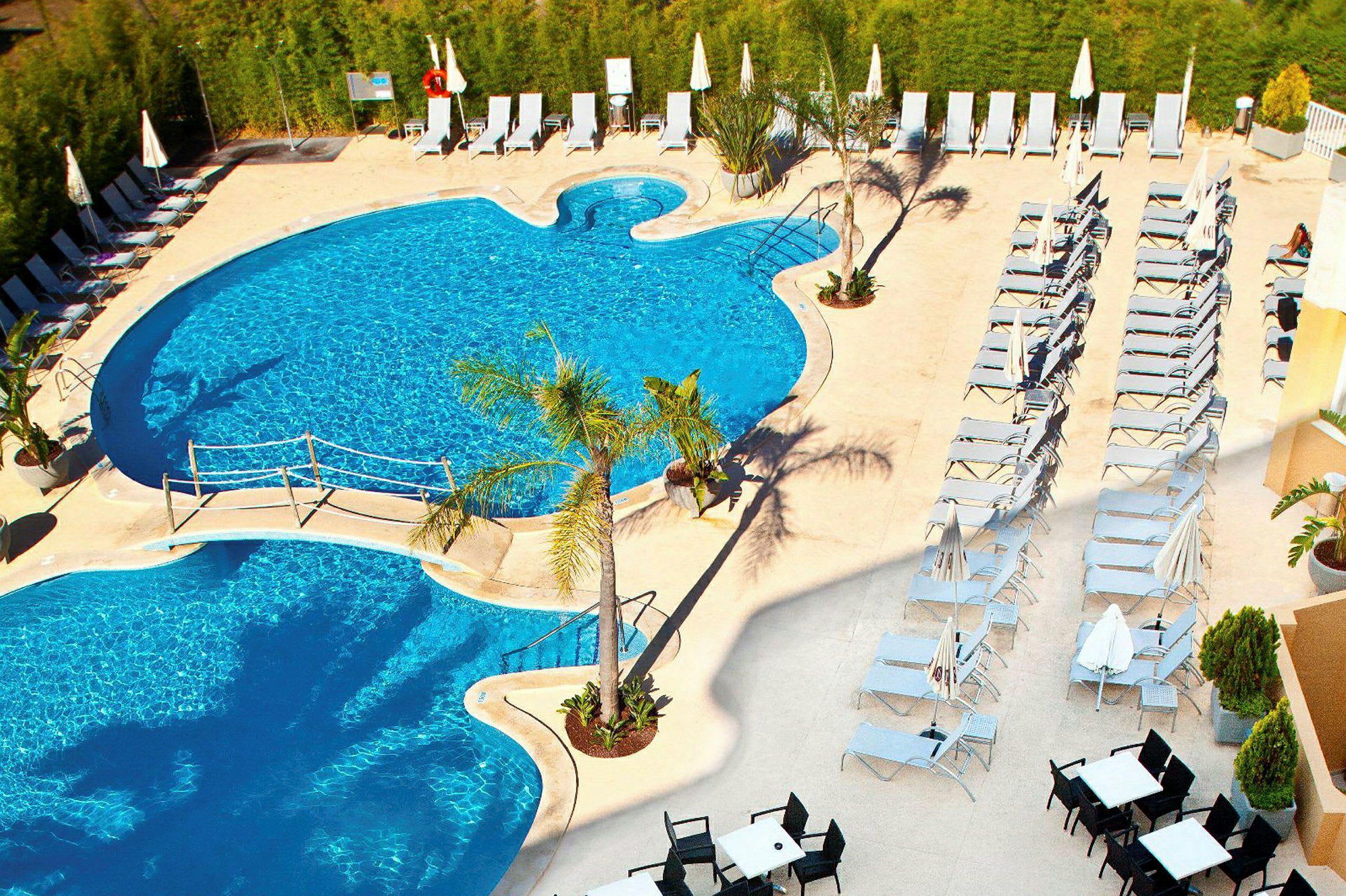 Udendørs pool med liggestole og parasoller på solterrassen. (AI-genereret tekst)