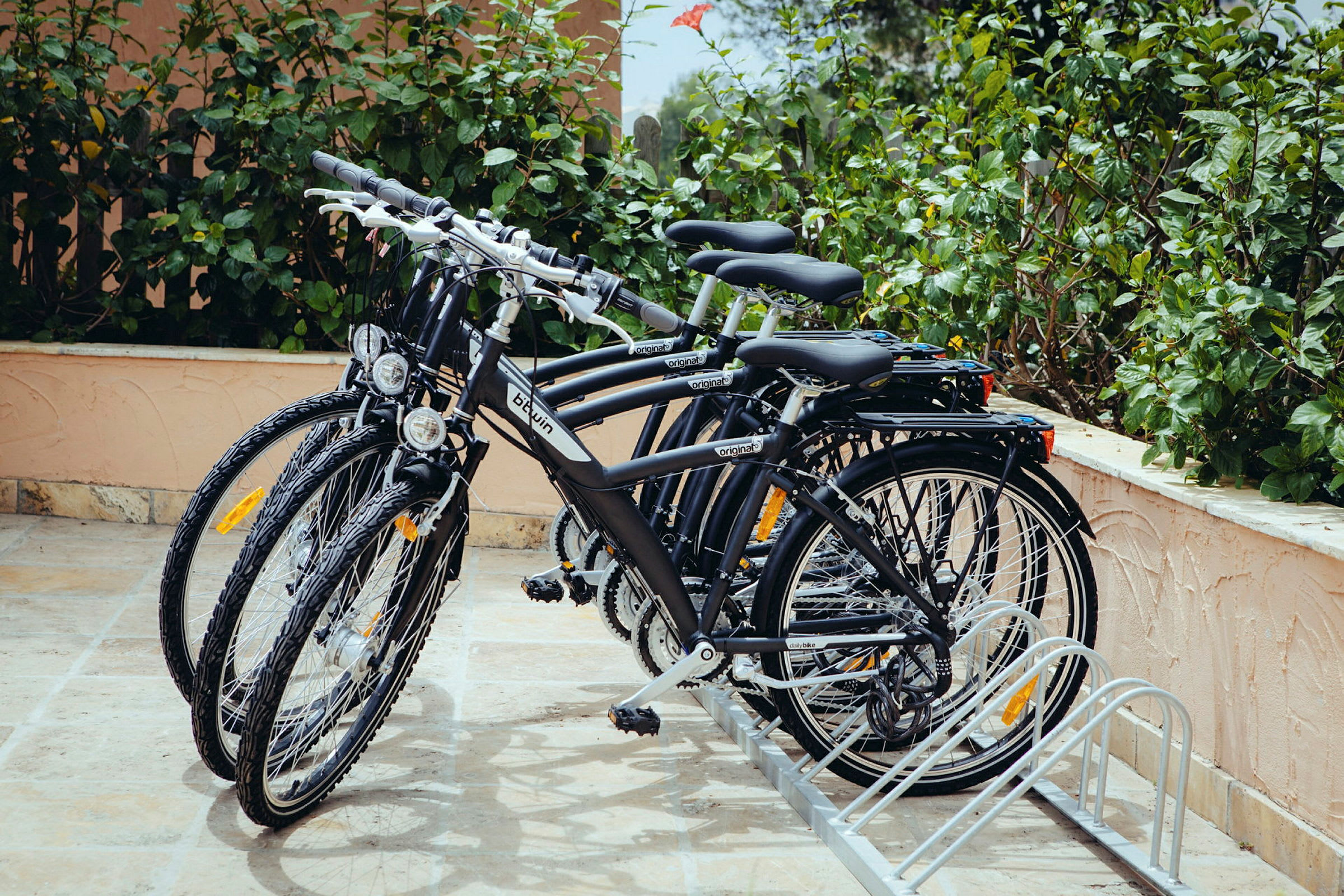Flere cykler parkeret i en cykelstativ ved en planteklædt væg. (AI-genereret tekst)