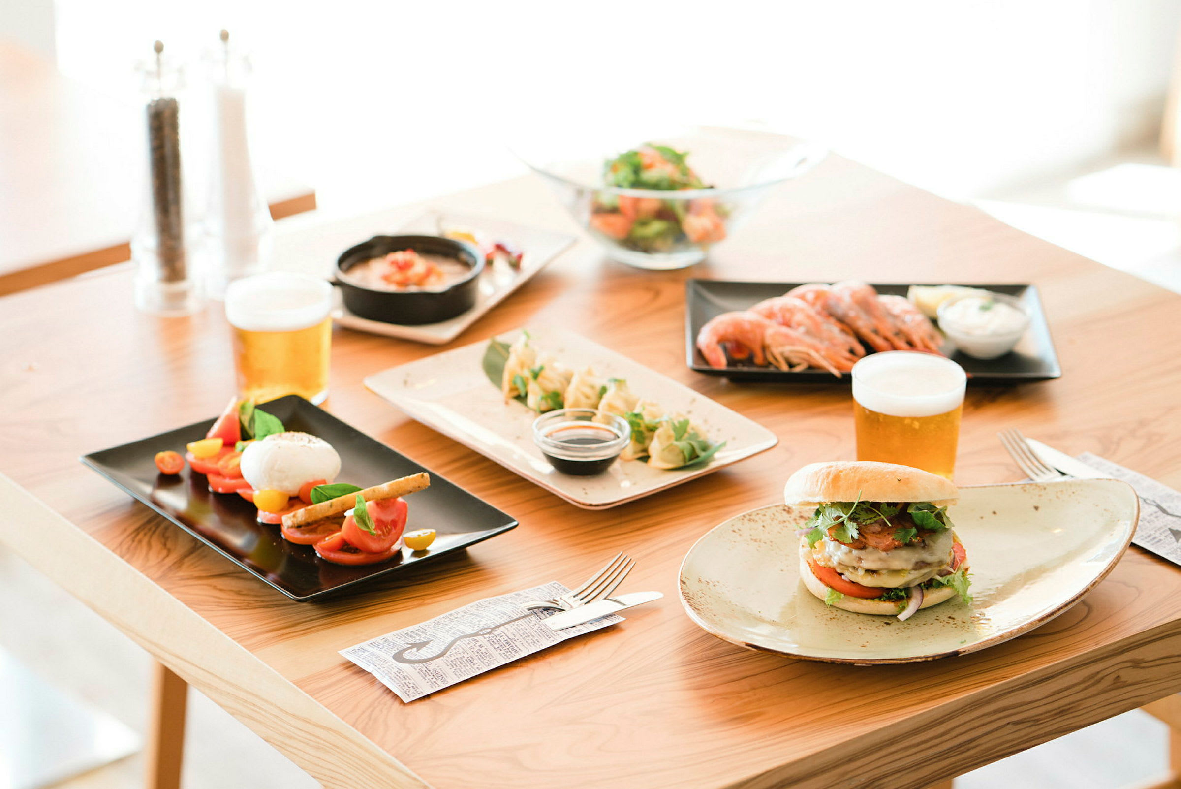 Et bord med forskellige retter og drikkevarer, herunder salat, rejer, burger og øl. (AI-genereret tekst)