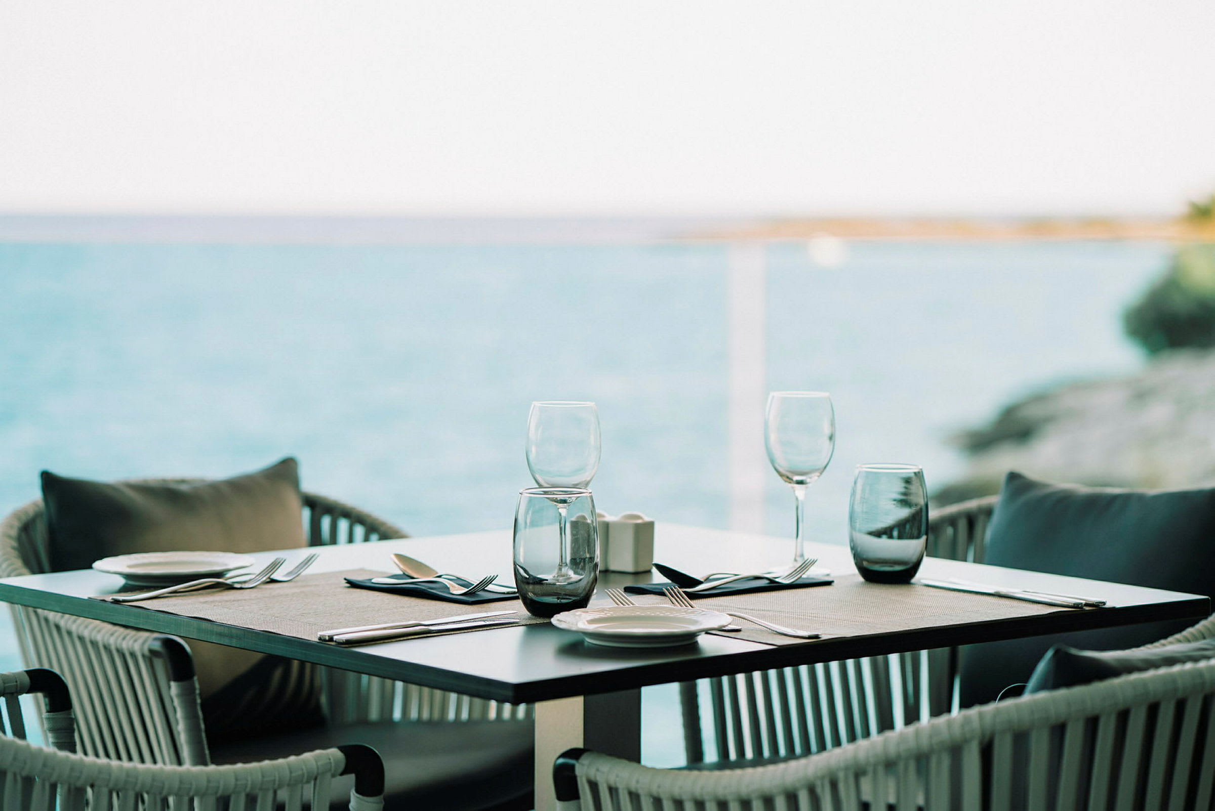 Et dækket bord med glas og bestik ved havet. (AI-genereret tekst)