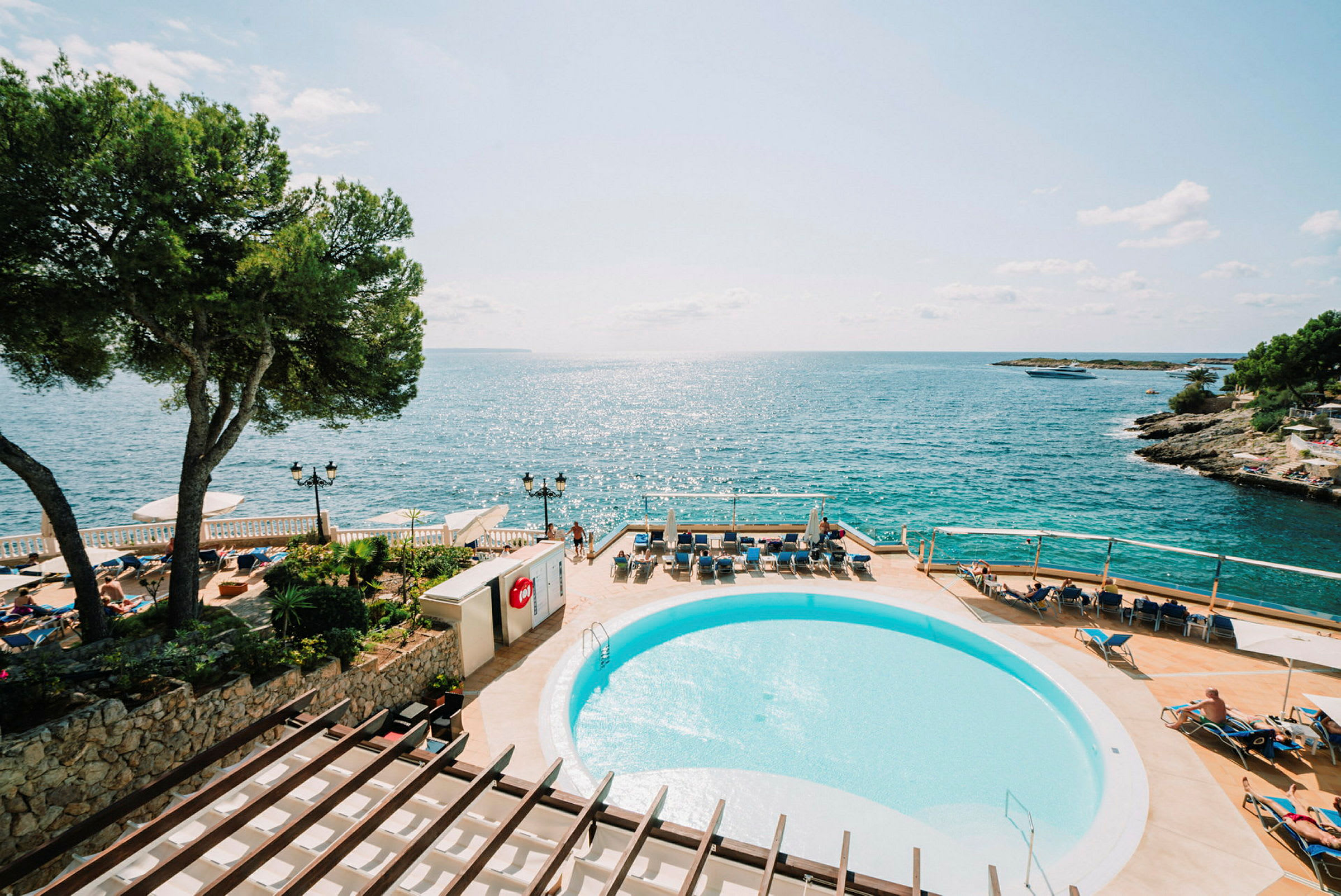 Udsigt over en solrig pool og terrasse med liggestole, med havet i baggrunden. (AI-genereret tekst)
