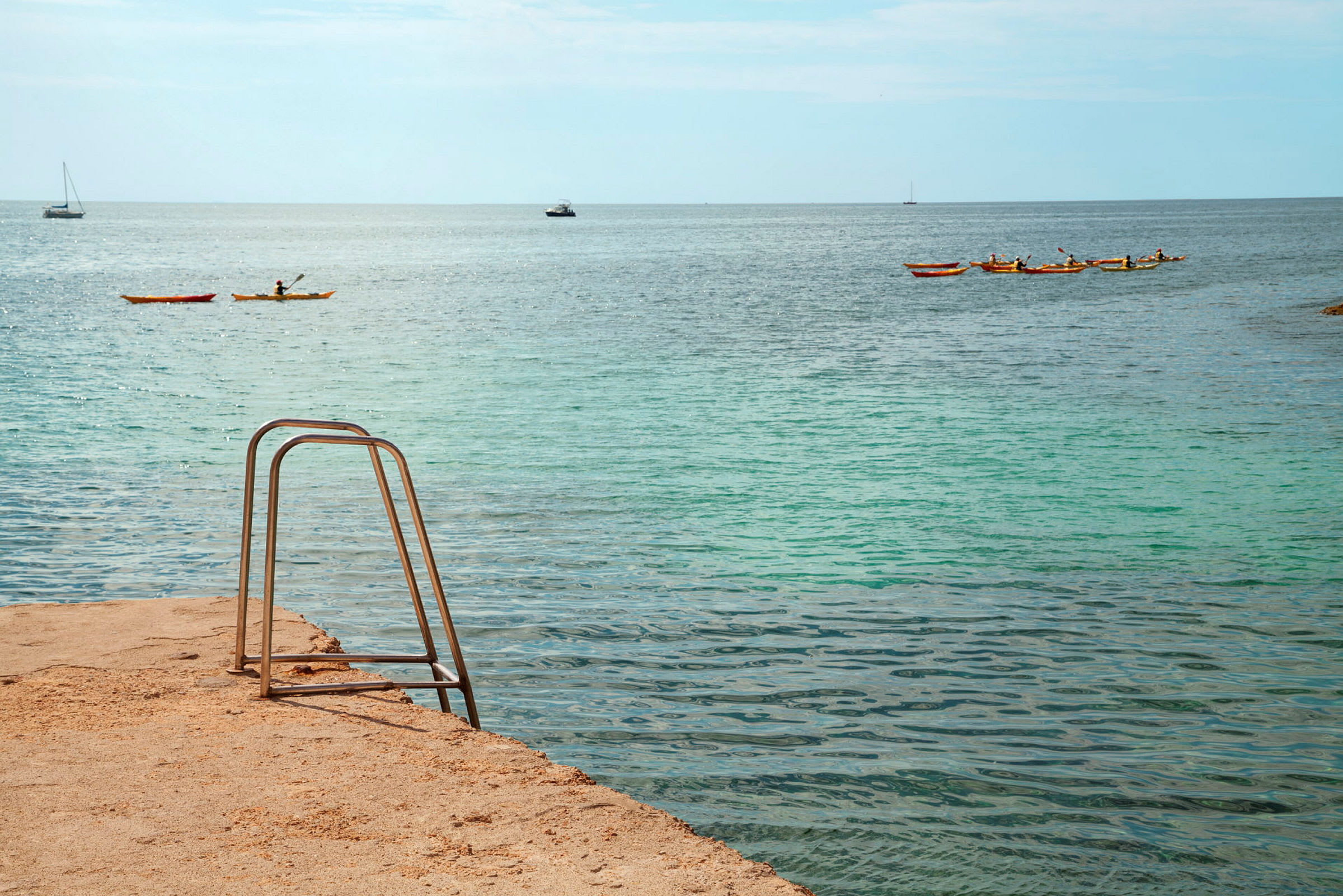 En badestige ved havet, med kajakker og både på vandet. (AI-genereret tekst)