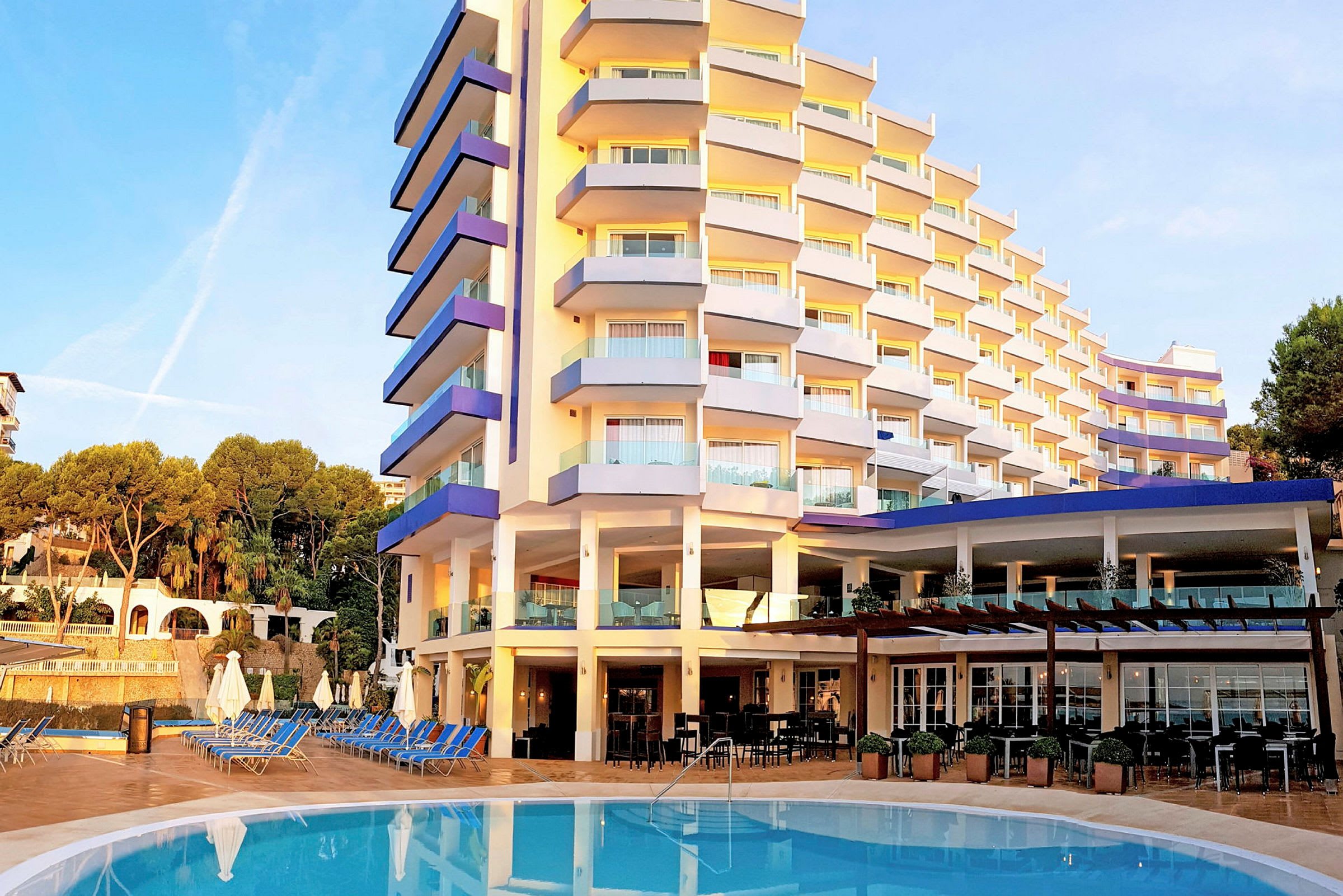 Et hotel med en pool foran og liggestole omkring. (AI-genereret tekst)