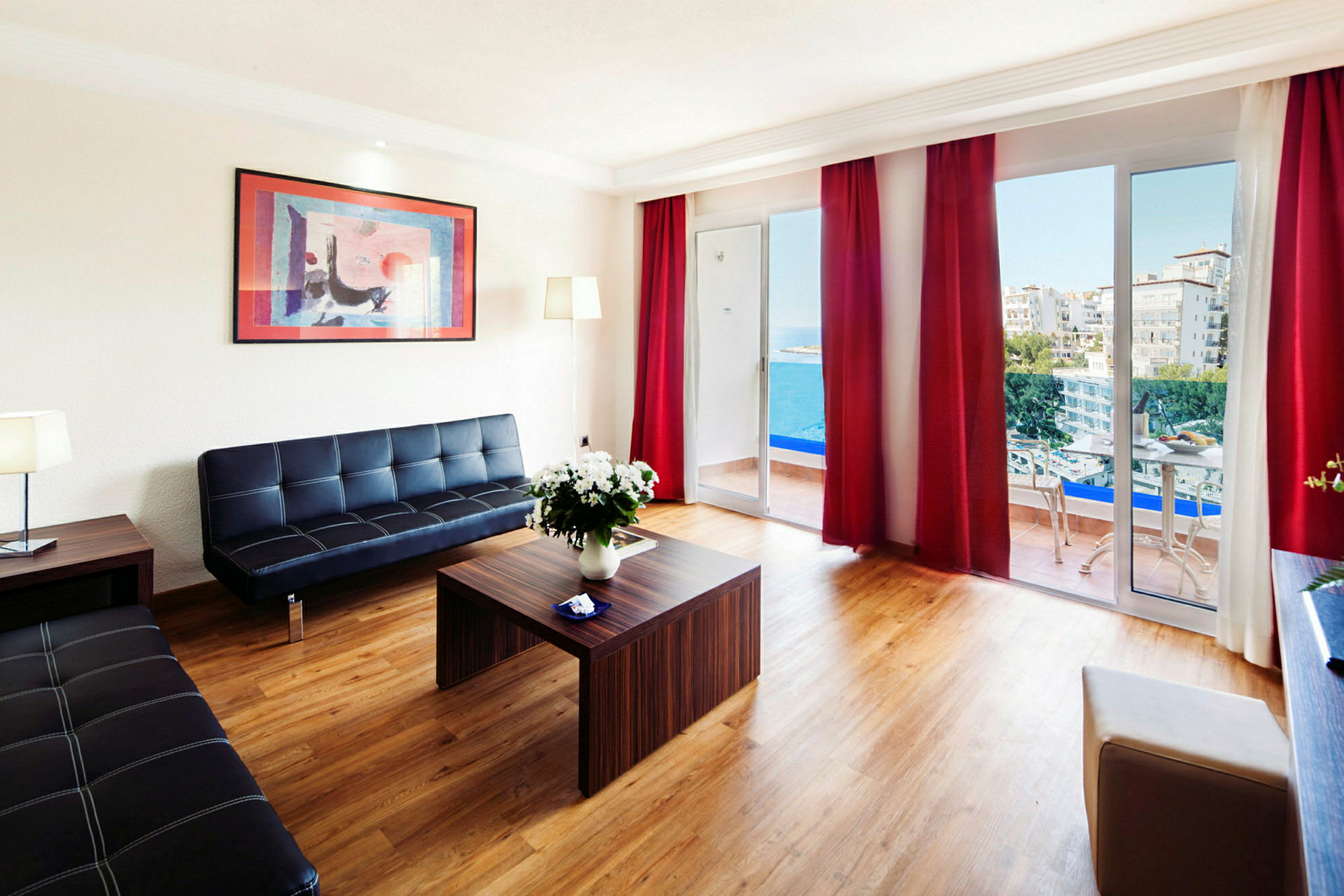 En moderne stue med udsigt til havet gennem store vinduer og balkon, møbleret med sorte sofaer og et træbord. (AI-genereret tekst)