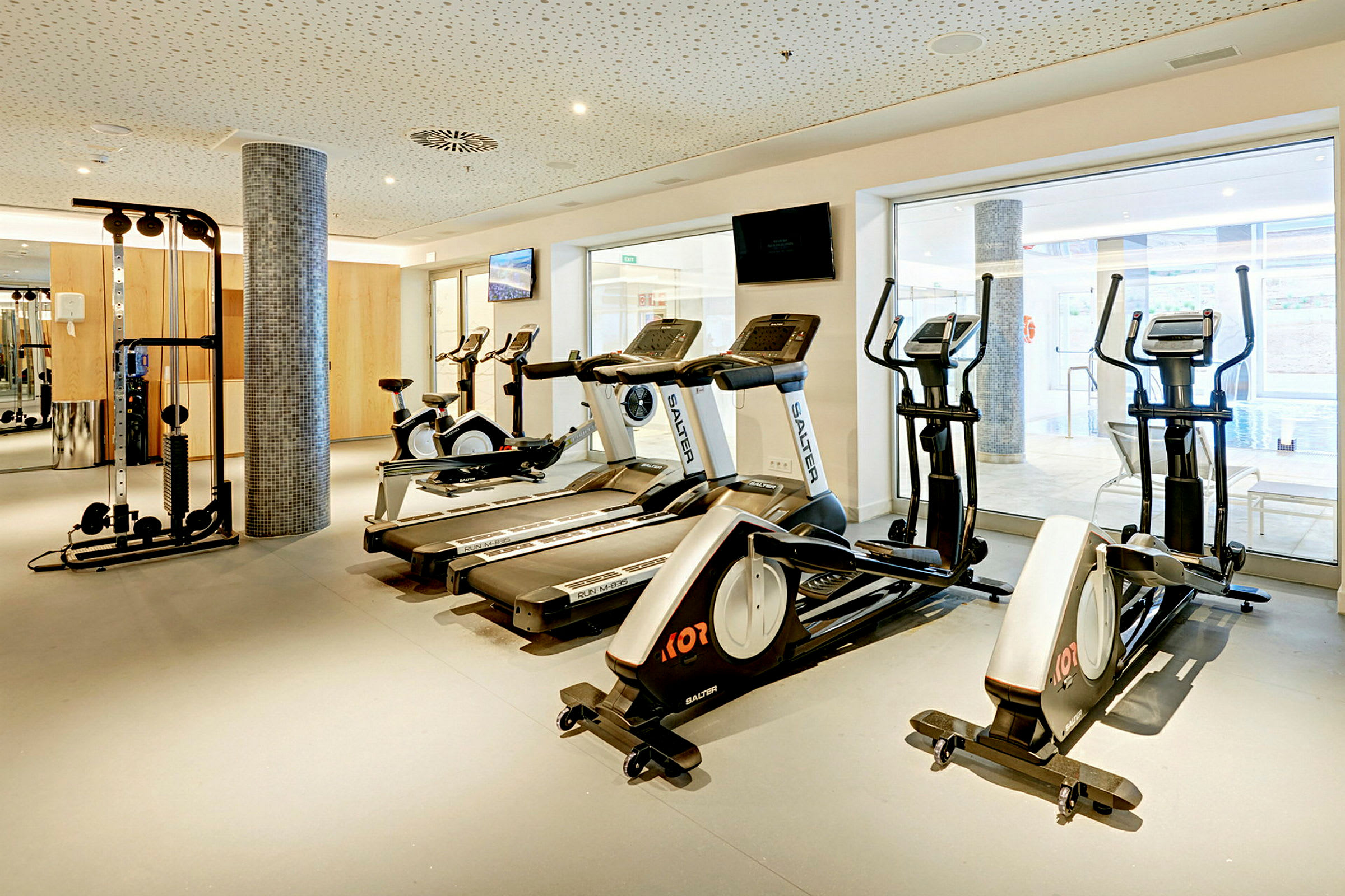 Et fitnesscenter med træningsmaskiner, herunder løbebånd, cykler og en kabelstation. (AI-genereret tekst)