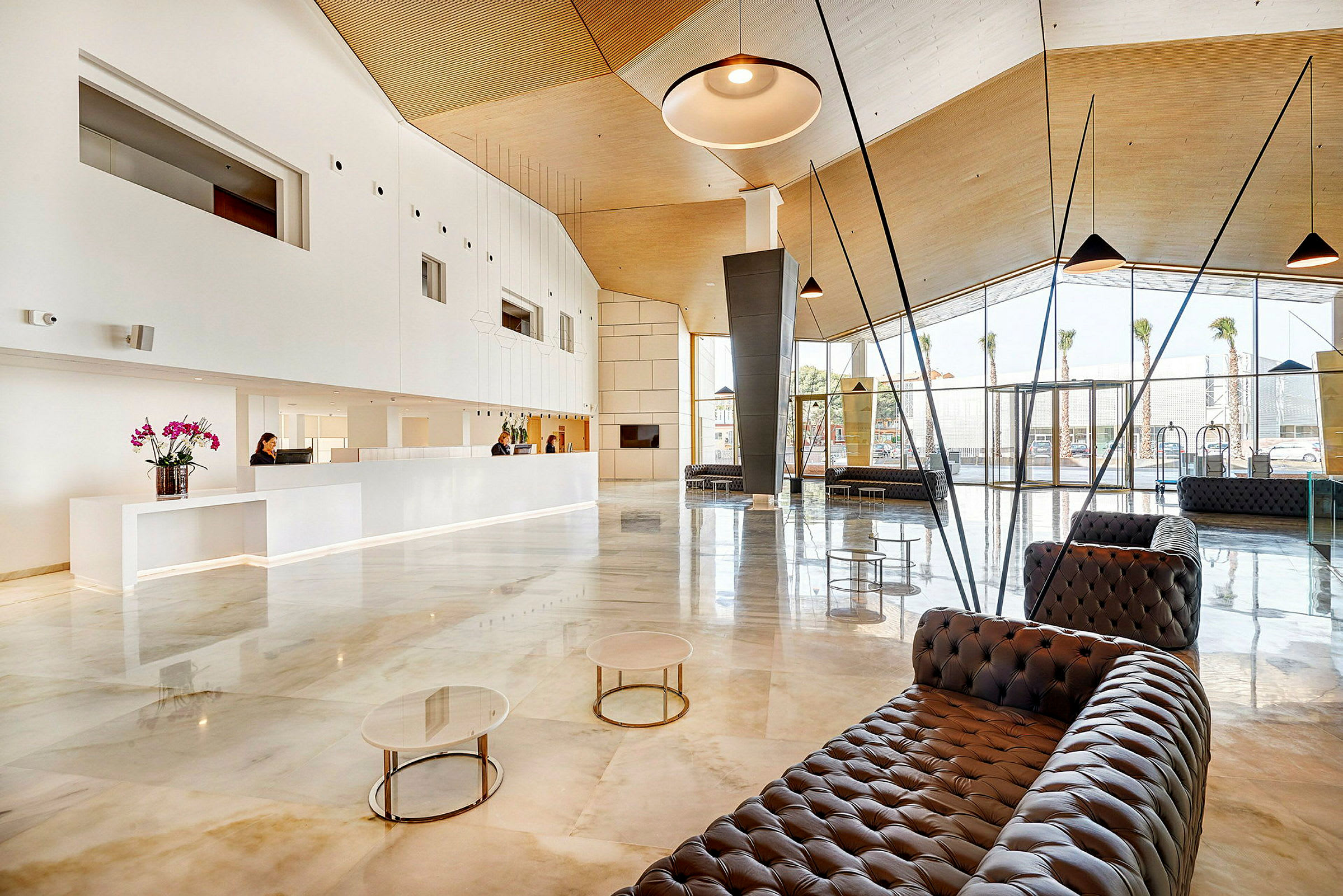 Hotellobby med moderne indretning, store vinduer og reception. (AI-genereret tekst)