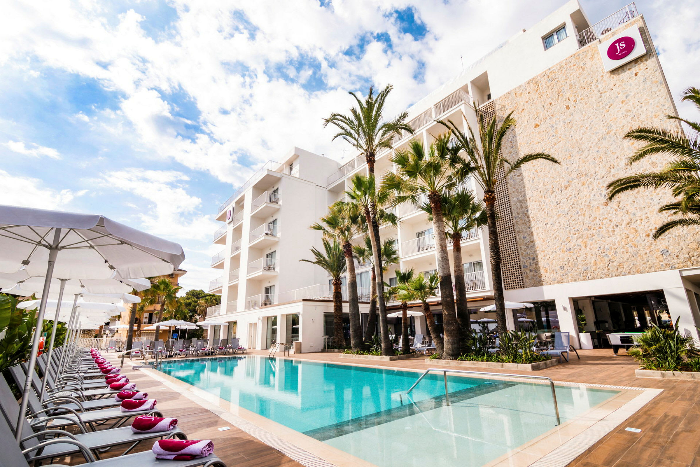 Udendørs swimmingpool med liggestole og et hotel i baggrunden. (AI-genereret tekst)