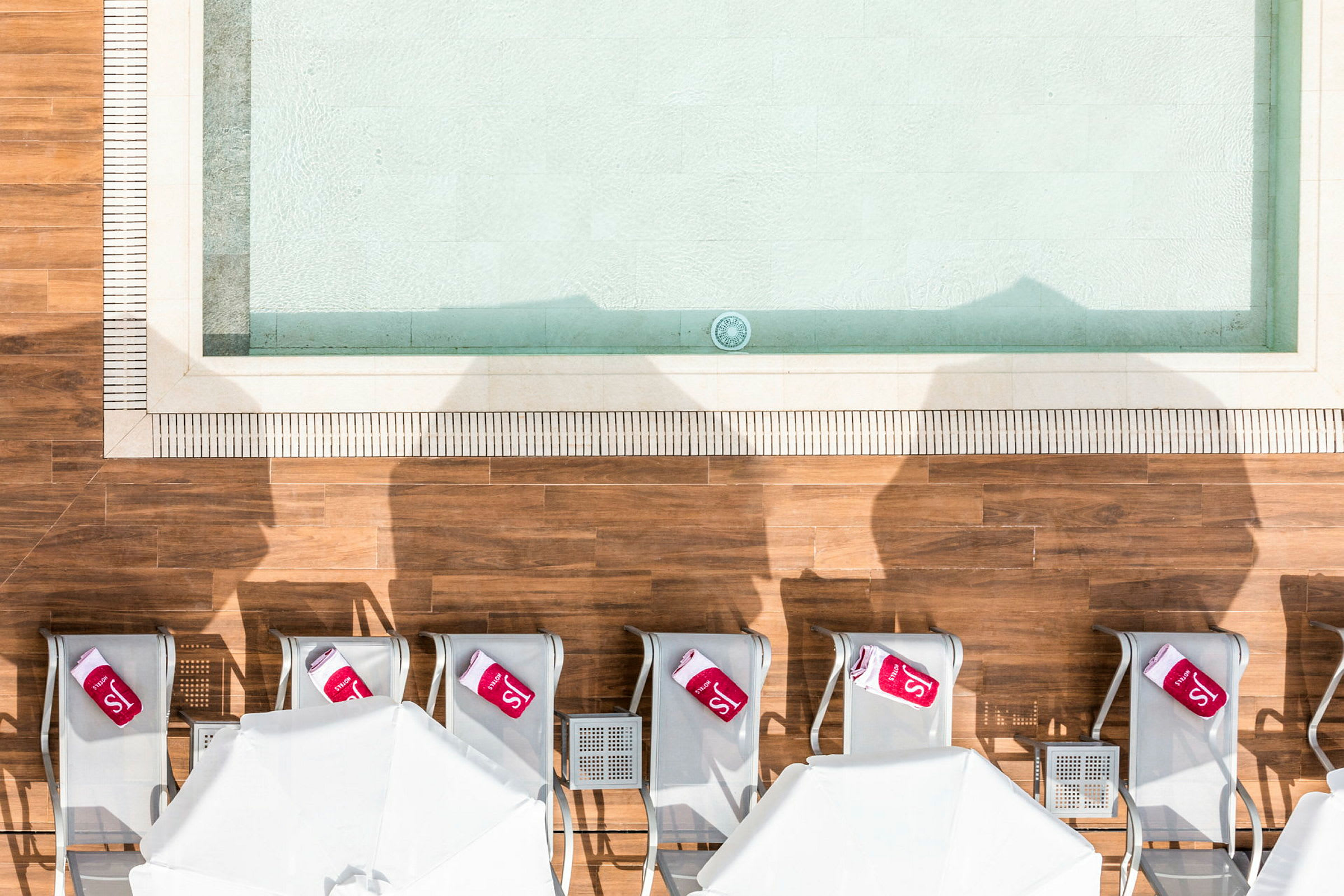 Udsigt ovenfra af liggestole og parasoller ved en swimmingpool. (AI-genereret tekst)