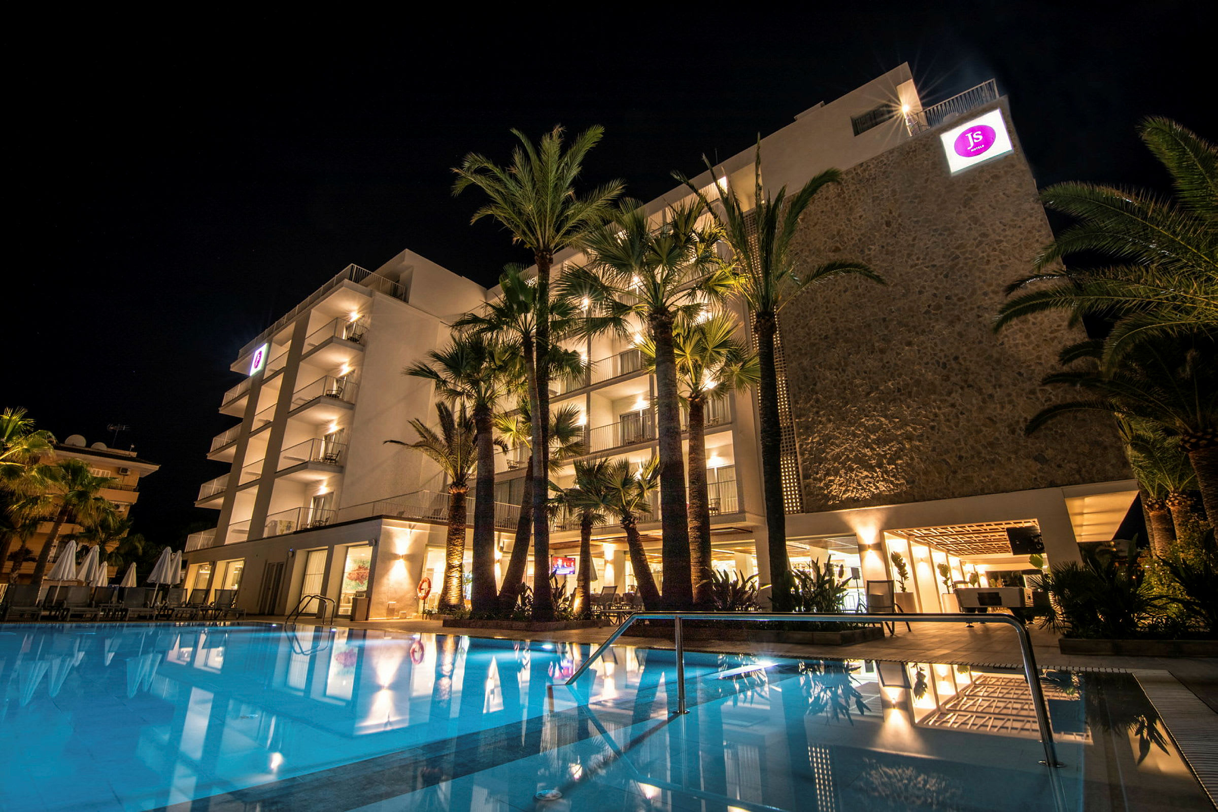 Hotelbygning med oplyst facade og en pool om aftenen. (AI-genereret tekst)