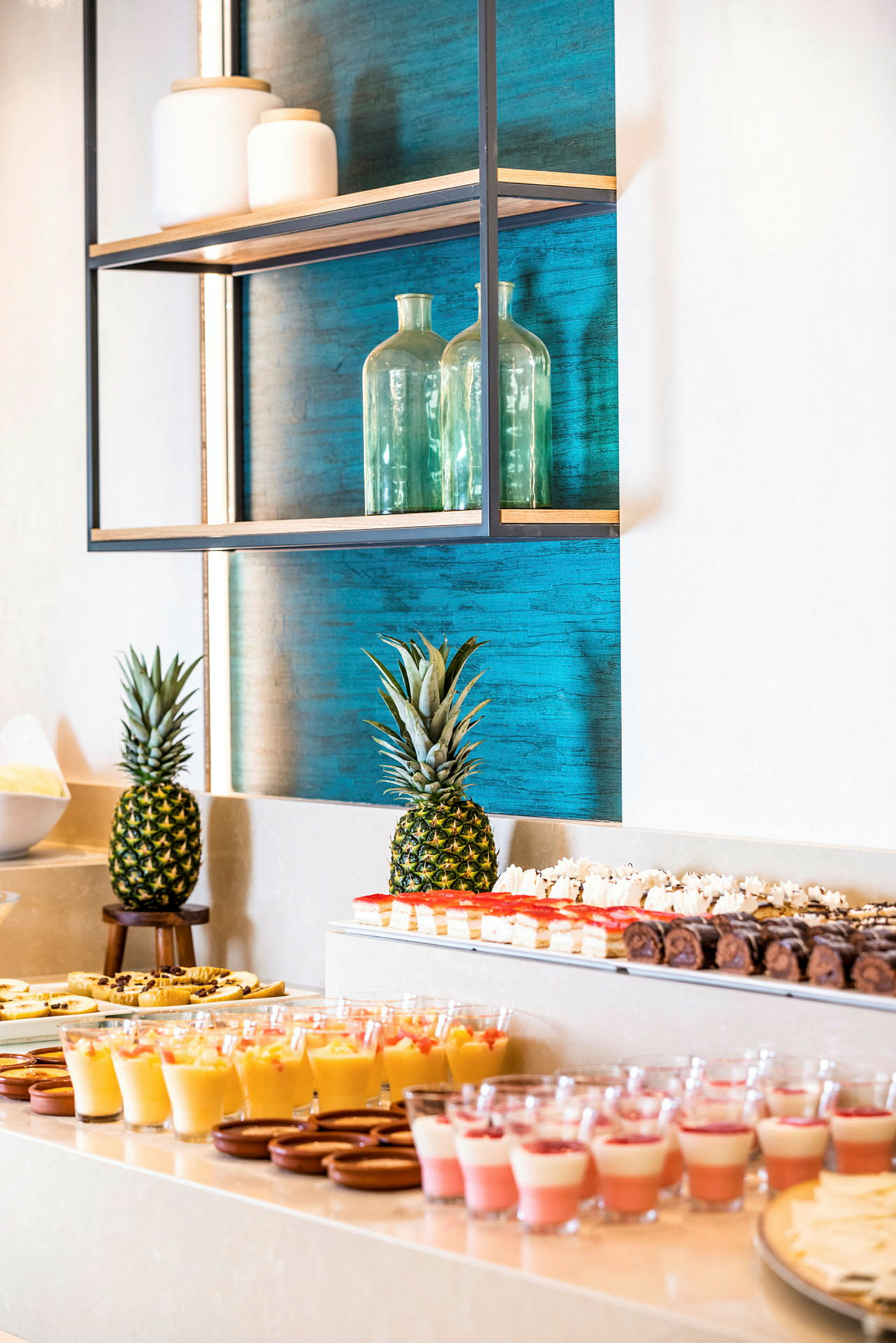Et bord med desserter og to ananas foran en blå baggrund. (AI-genereret tekst)