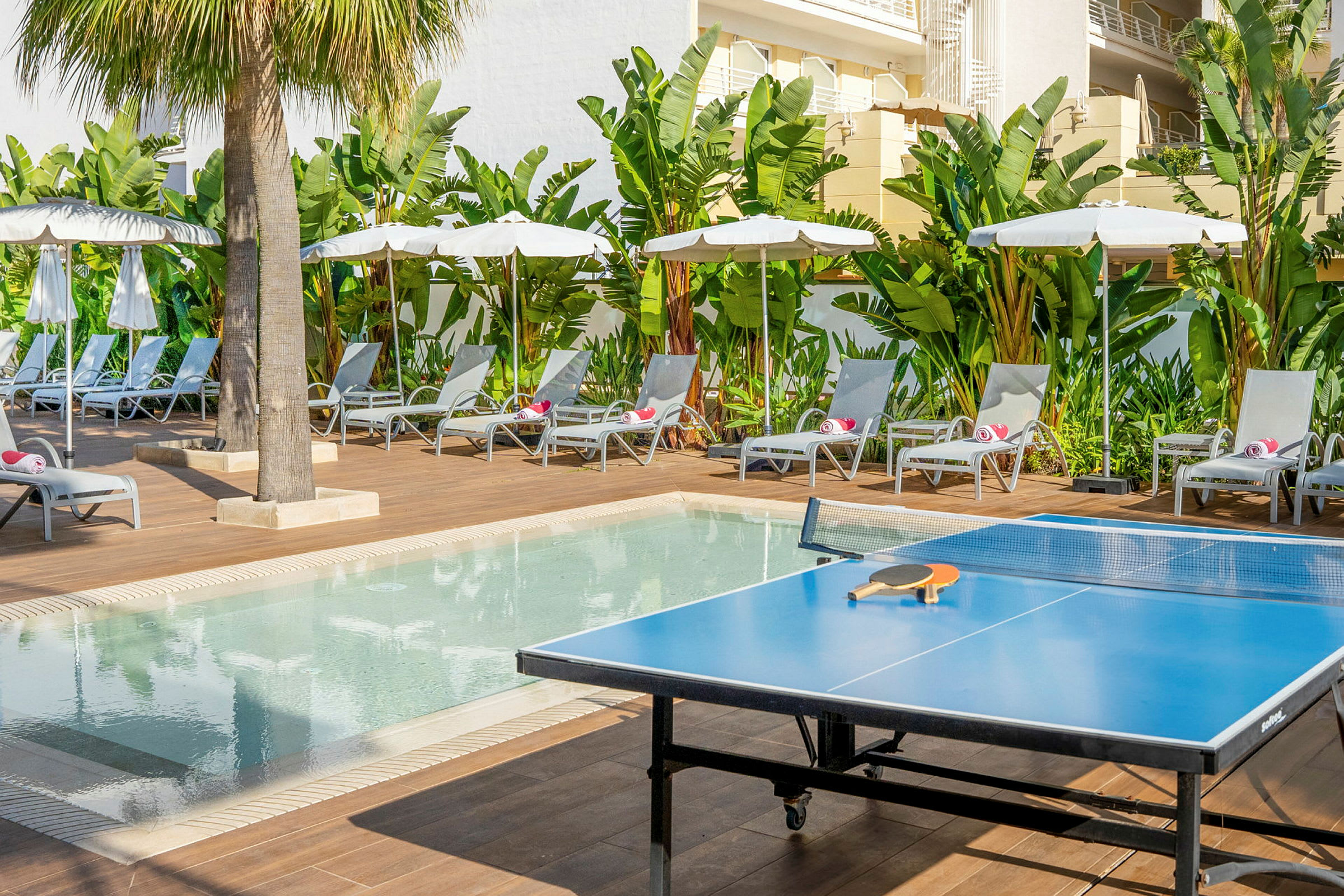 Et bordtennisbord ved en pool med solsenge og parasoller. (AI-genereret tekst)