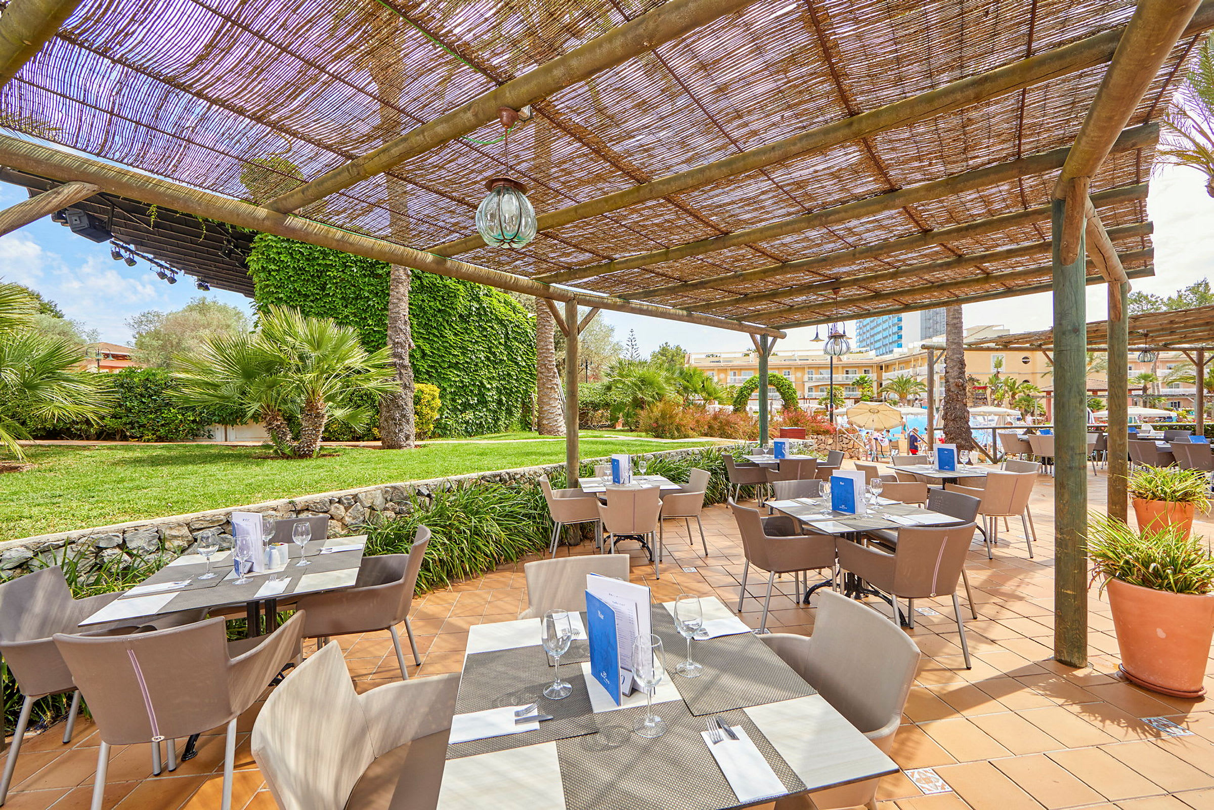 En udendørs restaurant med solbeskyttelse i en frodig havemiljø. (AI-genereret tekst)