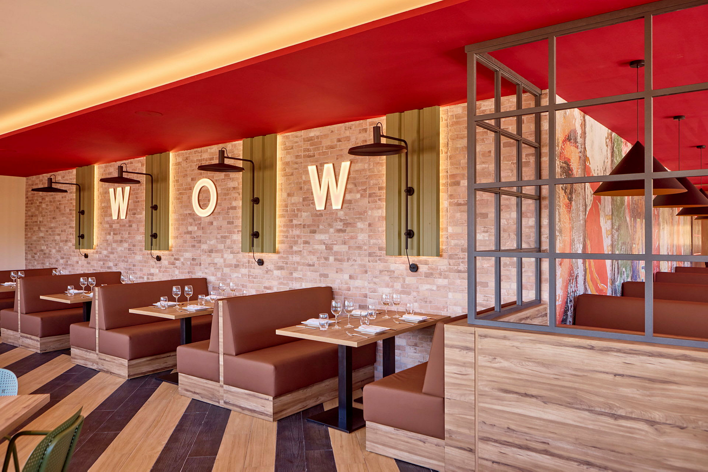 Restaurantmiljø med brune siddepladser, træborde og murstensvæg dekoreret med bogstaverne "WOW". (AI-genereret tekst)