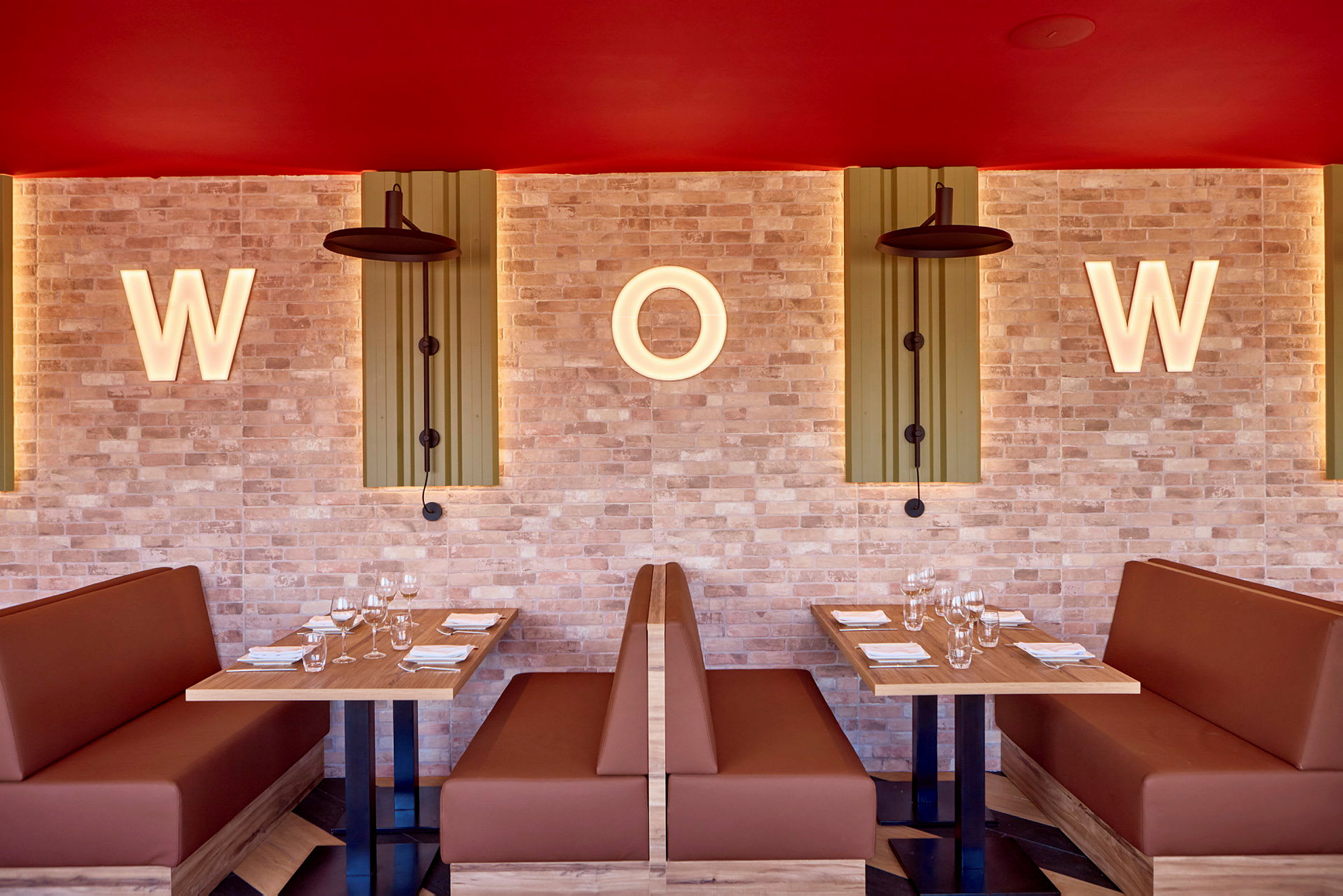To siddepladser med borde og sofaer i en restaurant, med belyste bogstaver "W" og "O" på en murstensvæg. (AI-genereret tekst)
