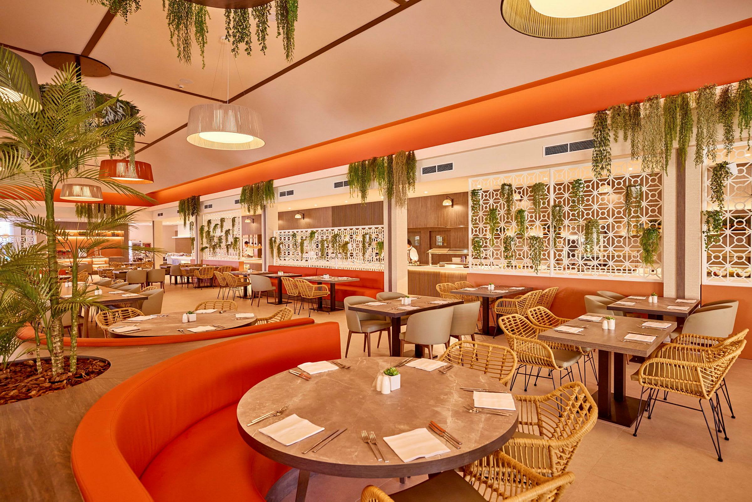 En restaurant med orange sofaer, flettede stole og grønne planter. (AI-genereret tekst)