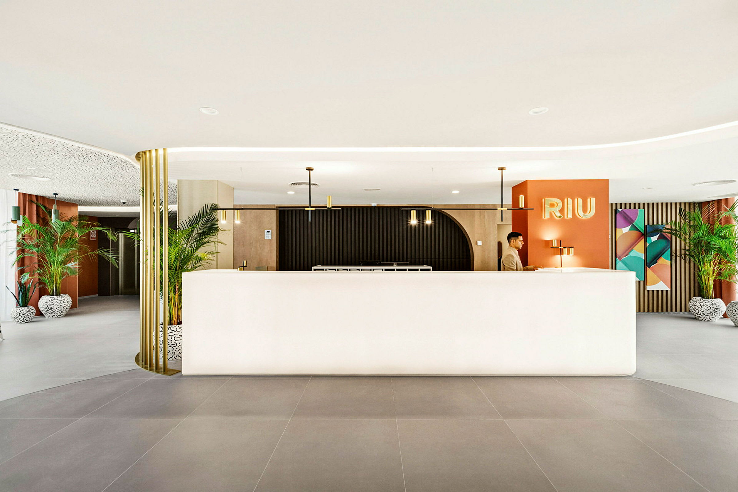Receptionen på et hotel med et moderne interiør, hvor planter, lamper og dekorationer omgiver en lys receptionsdisk. (AI-genereret tekst)