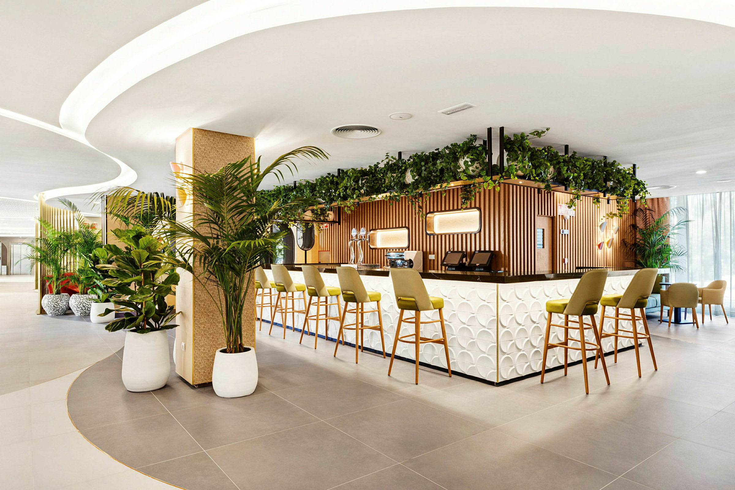 Billede af en moderne hotelbar med en stilfuld disk og grønne planter. Stole er opstillet ved bardisken. (AI-genereret tekst)