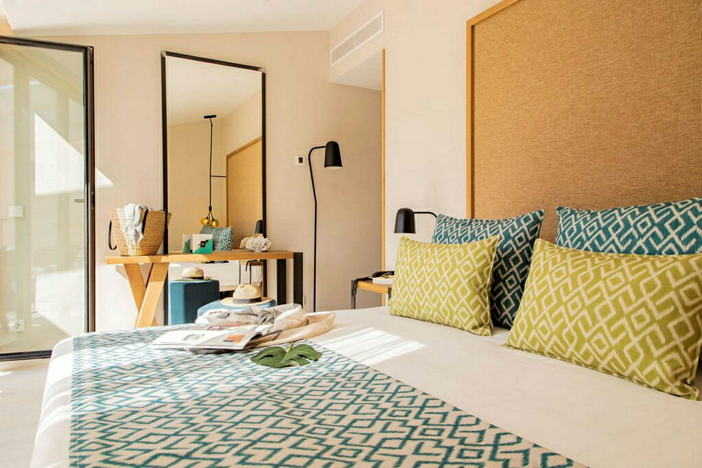 Hotelværelse med moderne indretning, seng med dekorative puder, spejl og skrivebord. (AI-genereret tekst)
