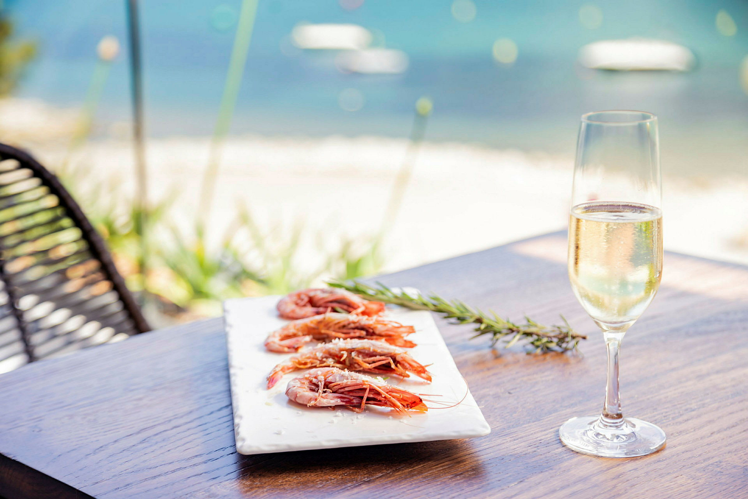 En tallerken med rejer og et glas champagne på et bord ved havet. (AI-genereret tekst)
