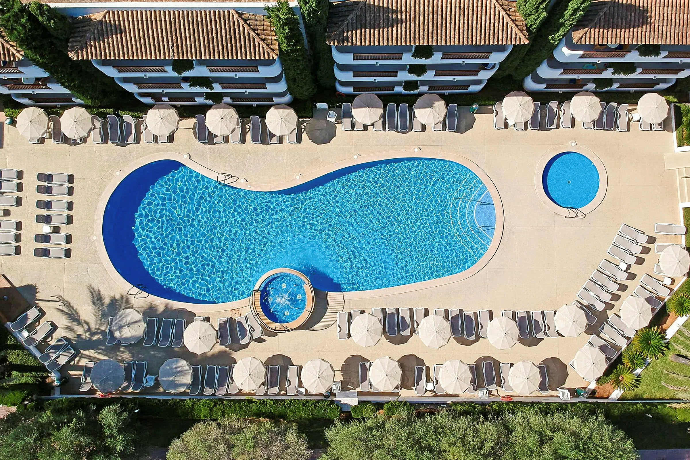 Luftfoto af en swimmingpool med liggestole og parasoller omkring. (AI-genereret tekst)