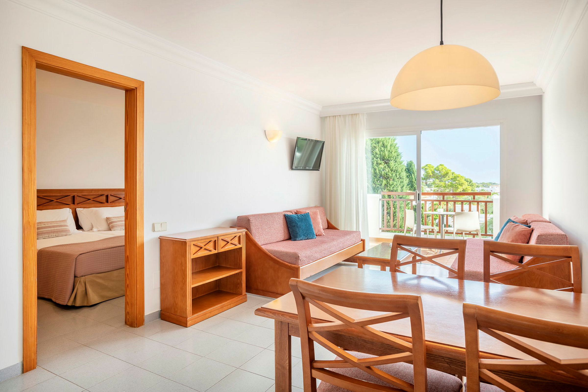 En hotelsuite med et bord, stole, sofa og et soveværelse synligt gennem en åben dør. (AI-genereret tekst)