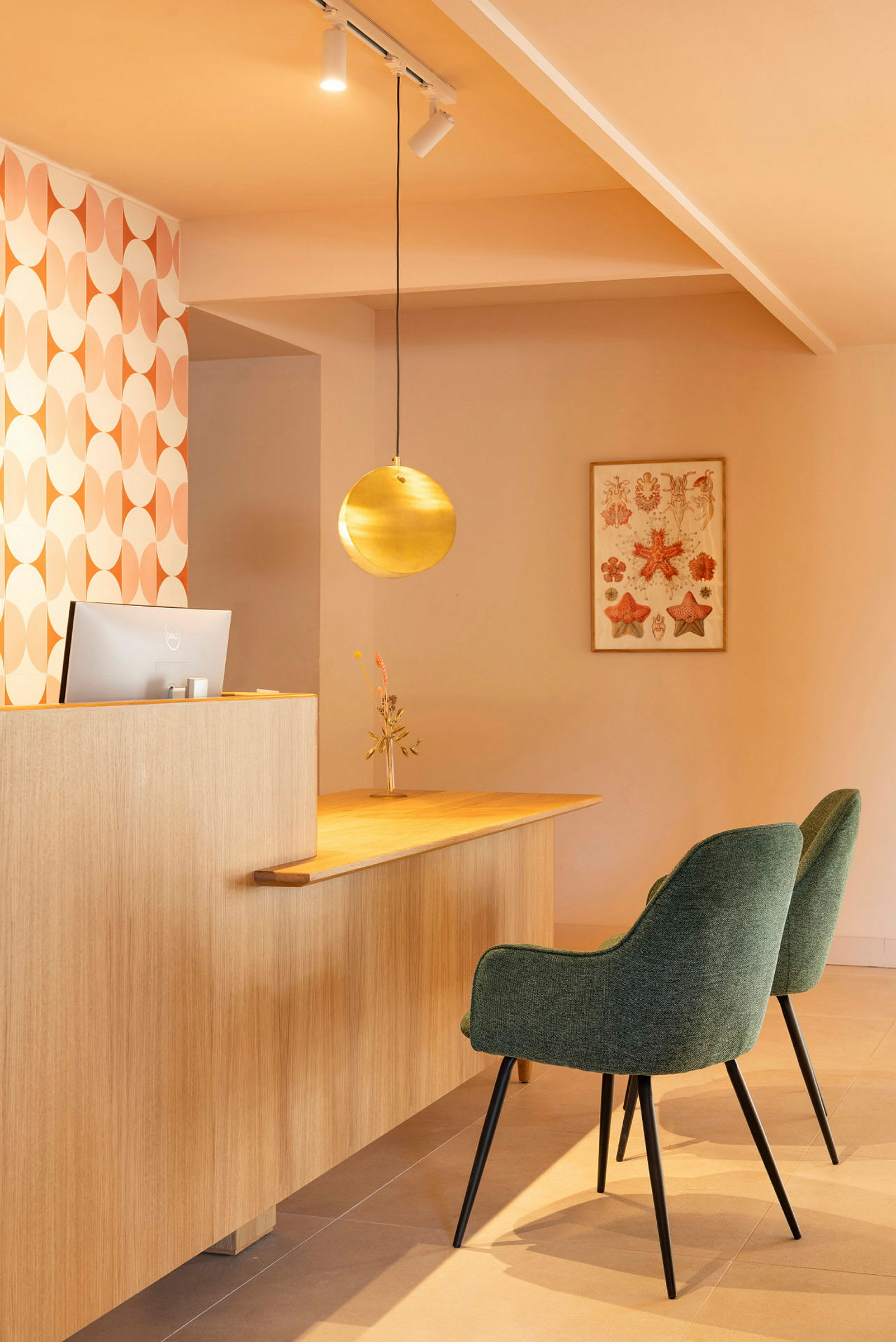 Billede af en receptionsdisk med to grønne stole, en metallisk rund lampe og vægdekoration. (AI-genereret tekst)