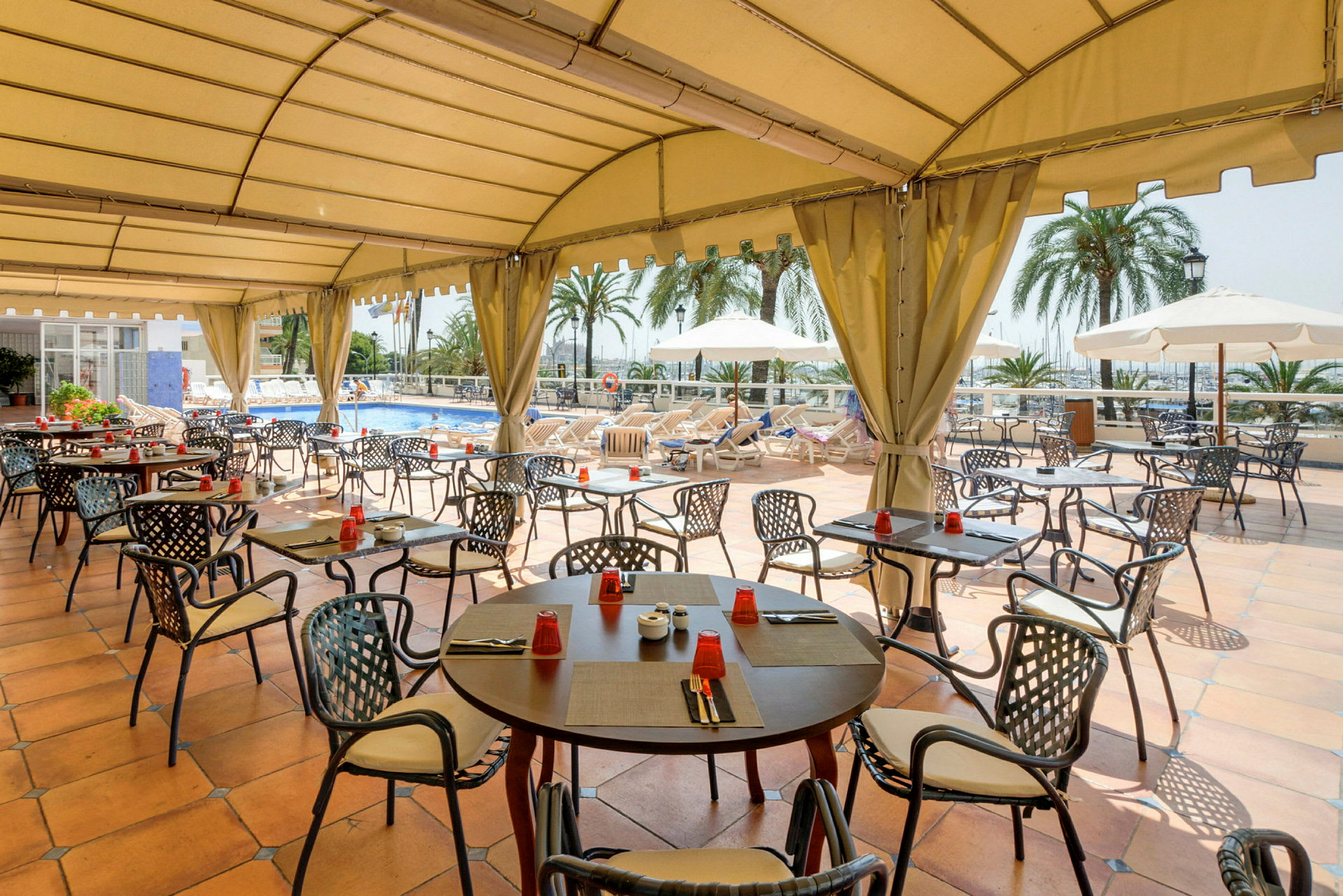 En restaurant terrasse med tag, hvor borde og stole er arrangeret omkring en pool. (AI-genereret tekst)