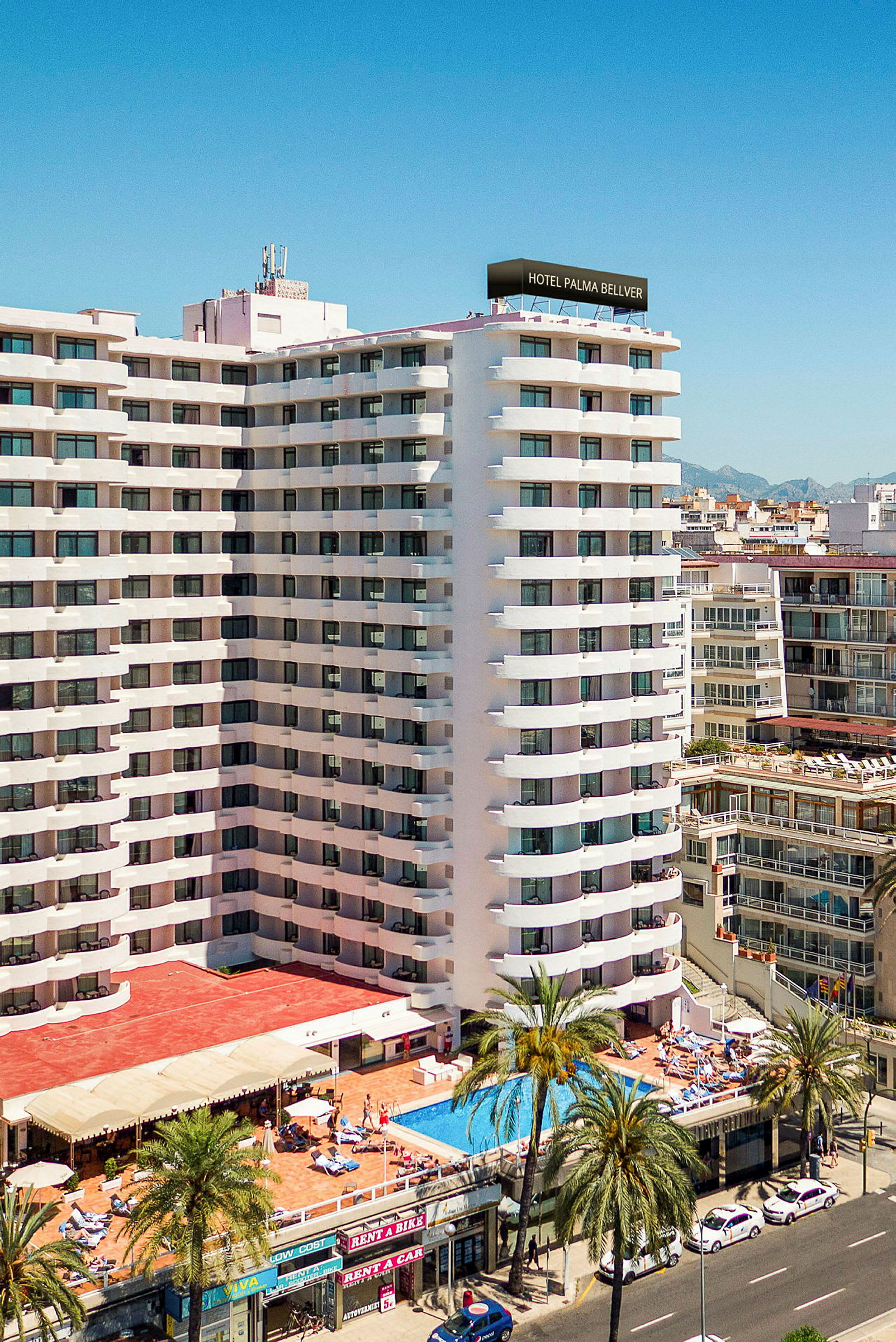Et hotel med hvid facade, poolområde og palmer i forgrunden. (AI-genereret tekst)