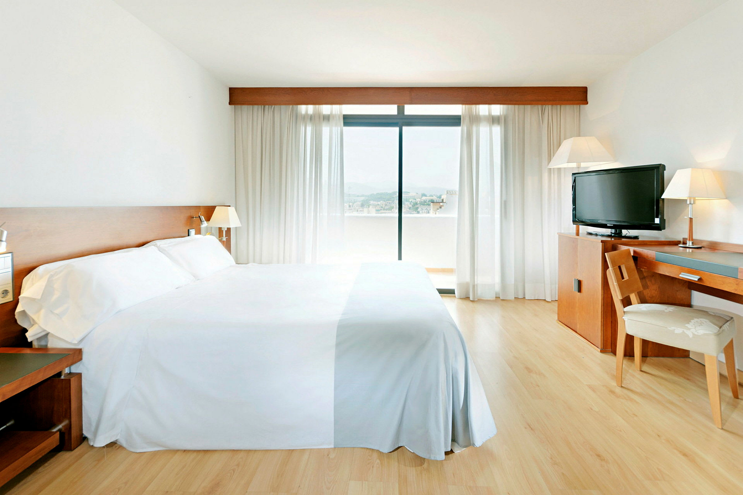 Hotelværelse med en stor seng, skrivebord, stol, tv og et vindue med udsigt. (AI-genereret tekst)