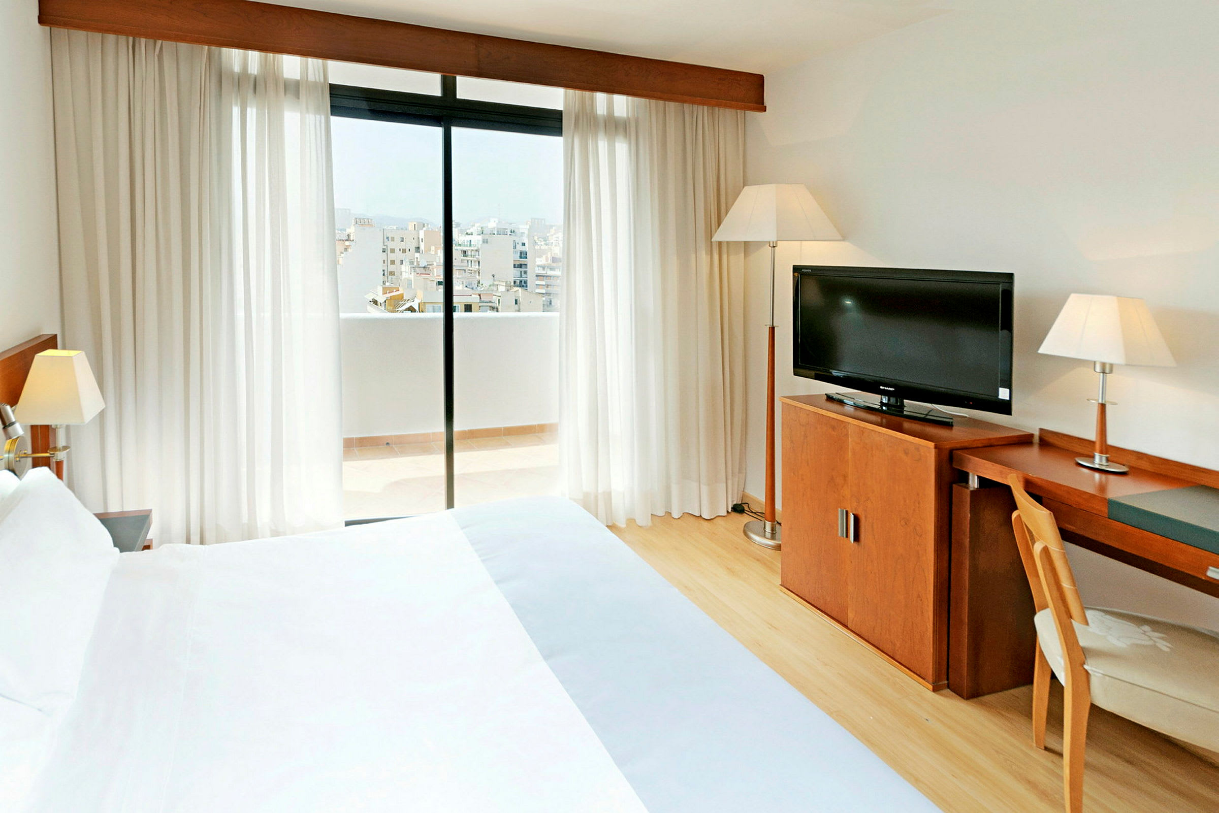 Et hotelværelse med en dobbeltseng, skrivebord, TV og en balkon med udsigt over byen. (AI-genereret tekst)