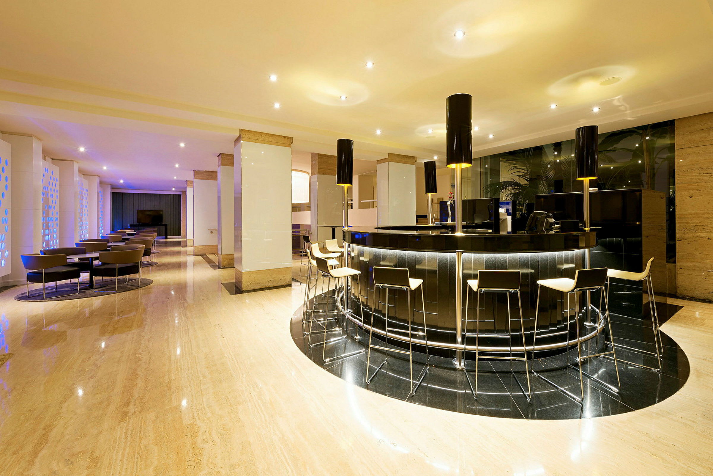 En moderne hotellobby med en elegant bardisk og barstole. Der er stole og borde placeret i baggrunden. (AI-genereret tekst)