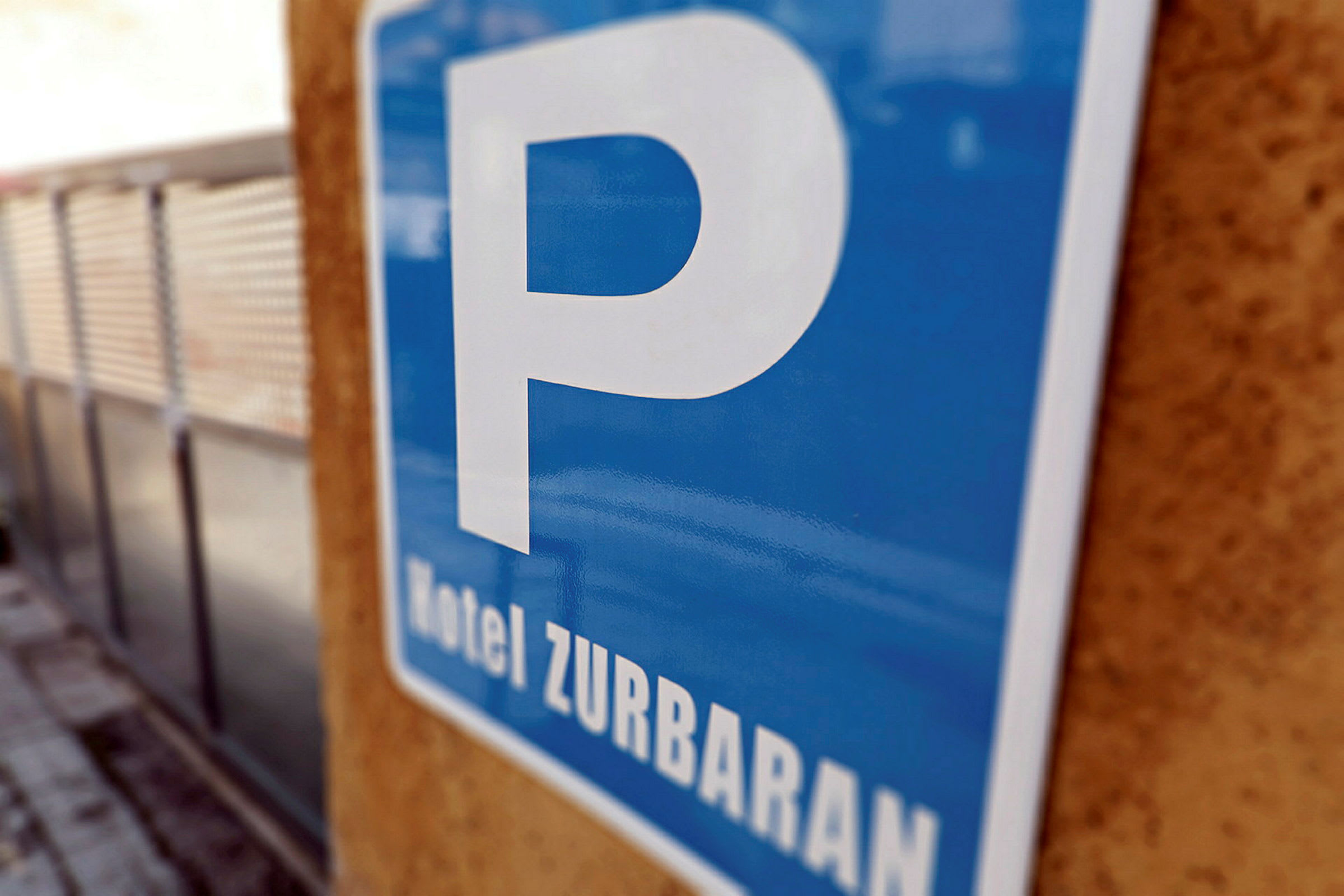 Et blåt parkeringsskilt med teksten 'Hotel Zurbaran', som hænger på en væg. (AI-genereret tekst)