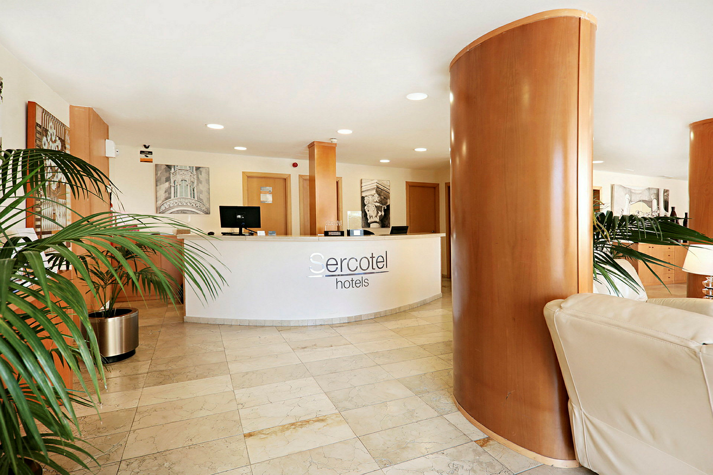 Receptionens skranke med Sercotel-hotellogo ses i en lobby med marmorgulv og dekorative planter. (AI-genereret tekst)